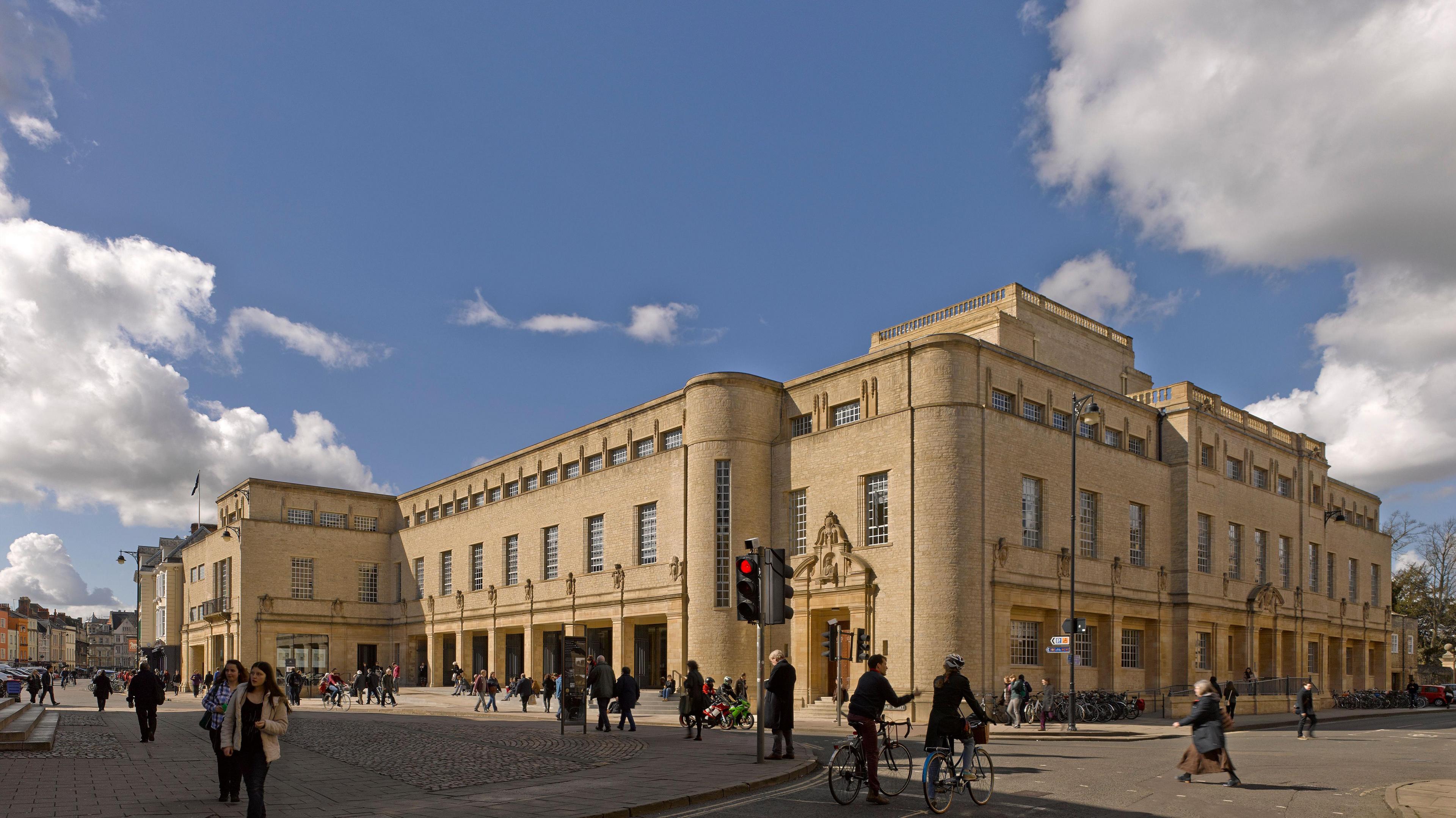 Exterior of the Weston Library on Broad Street. People are seen walking and riding bikes. It is a clear day.
