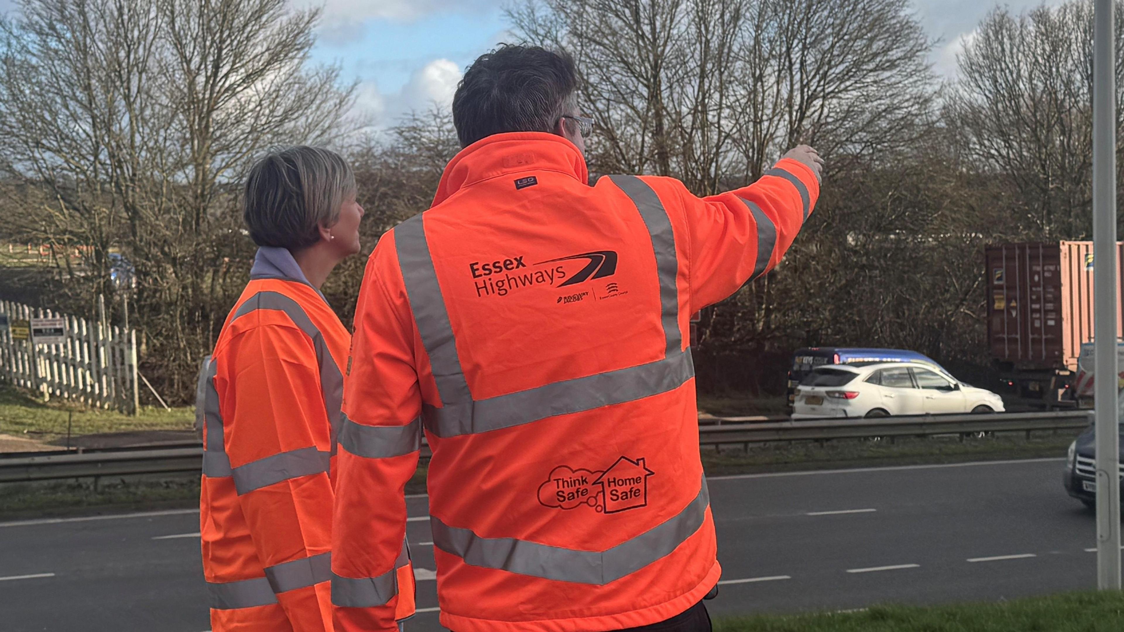 Man and woman in orange high vis on the side of a dual carriageway 