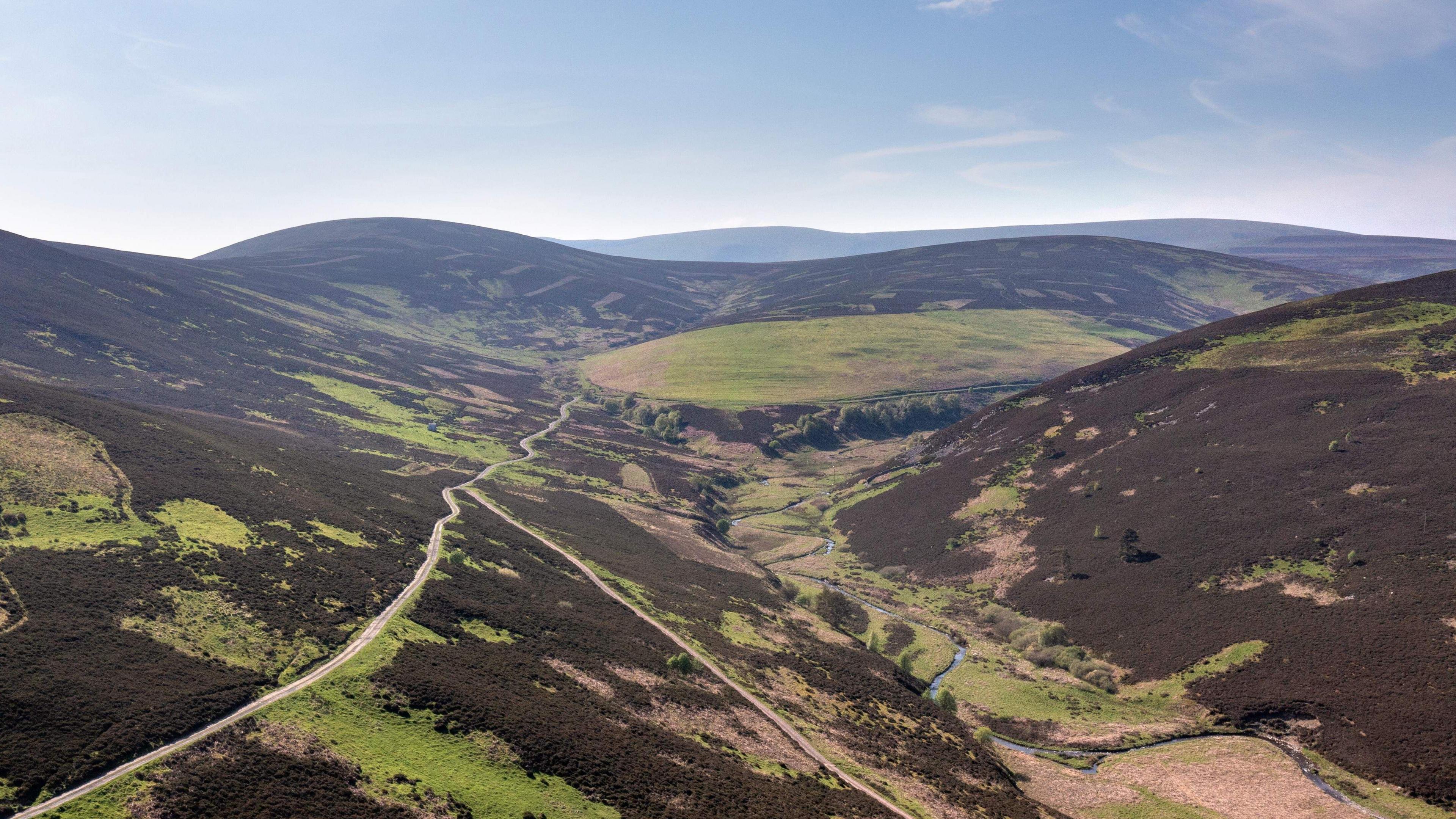 An aerial shot of a moorland valley with a stream slaloming through the middle of it.