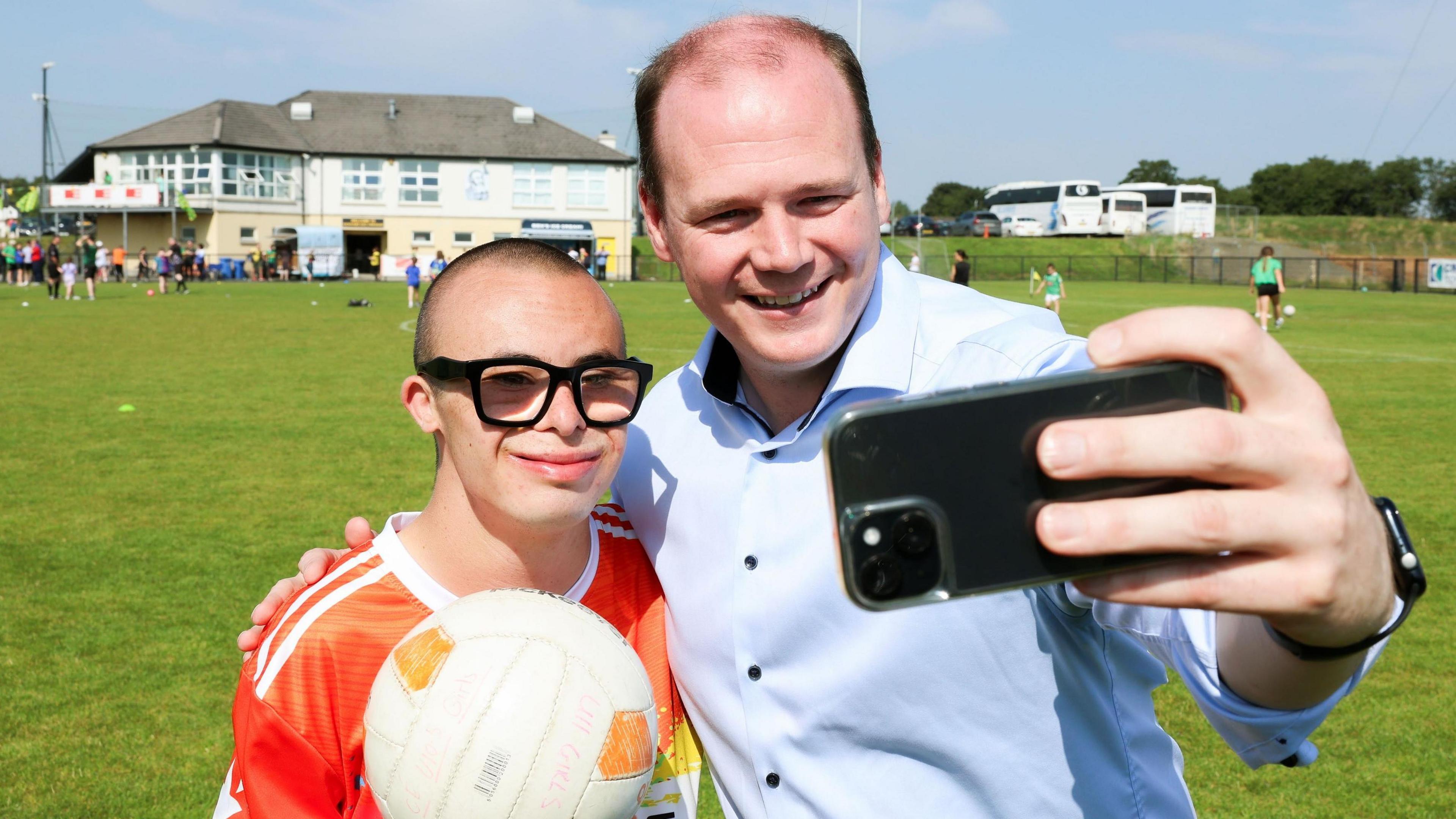 Gordon Lyons poses for a selfie with one of the young players.  He has his arm around the boy who is holding a football and smiling. 