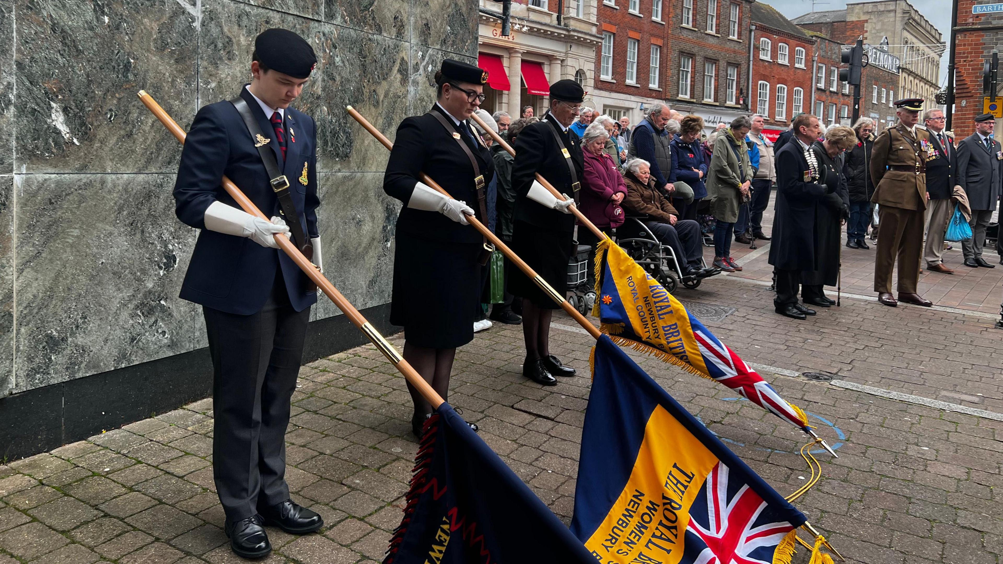 Three military cadets lower flags during a two minutes' silence in Newbury town centre as a crowd of people stand nearby