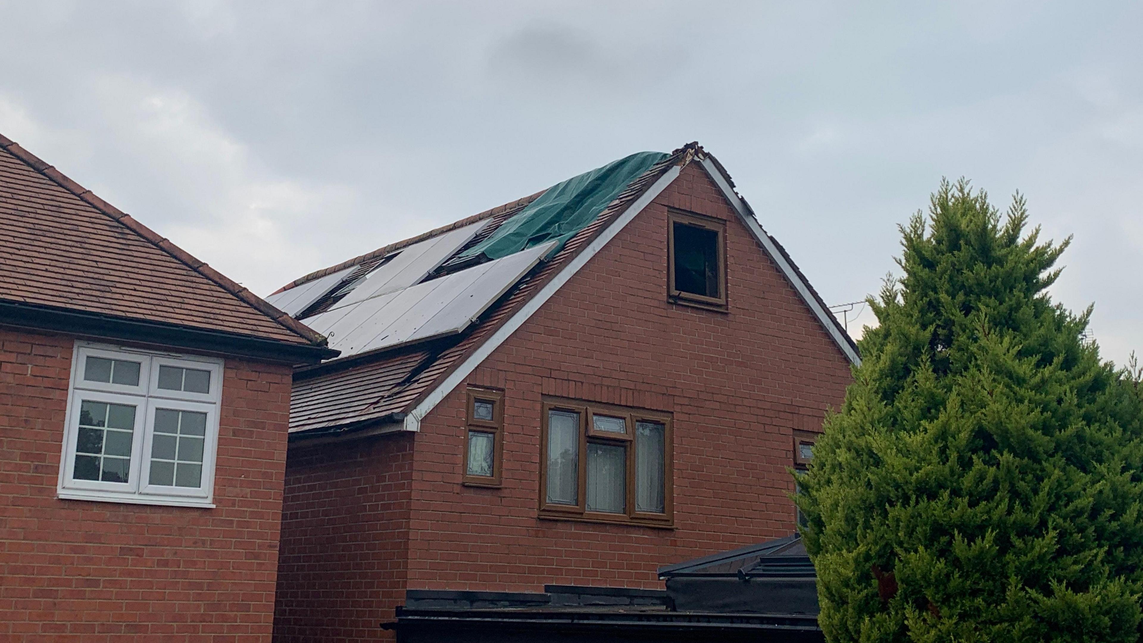 The top of a house showing a roof which has been damaged and patched up after a lightning strike caused it to set on fire. The top window, in the roof, is missing.