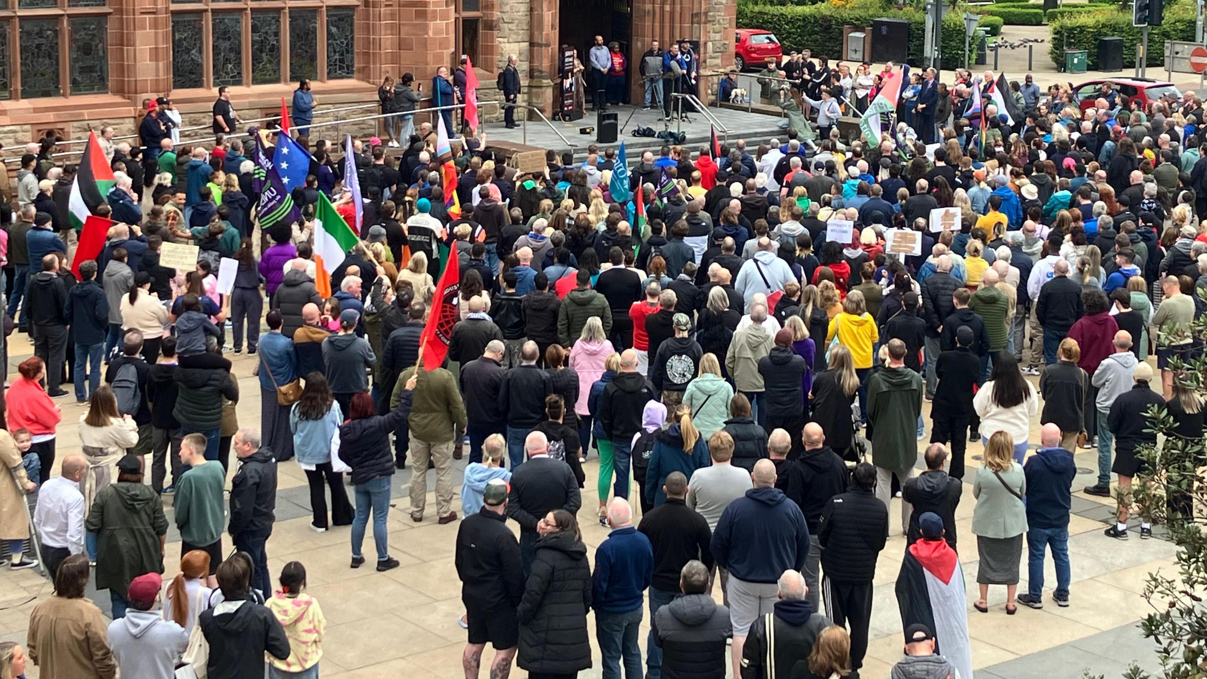 crowds with colourful flags, facing the Guildhall with speakers set up at the front 