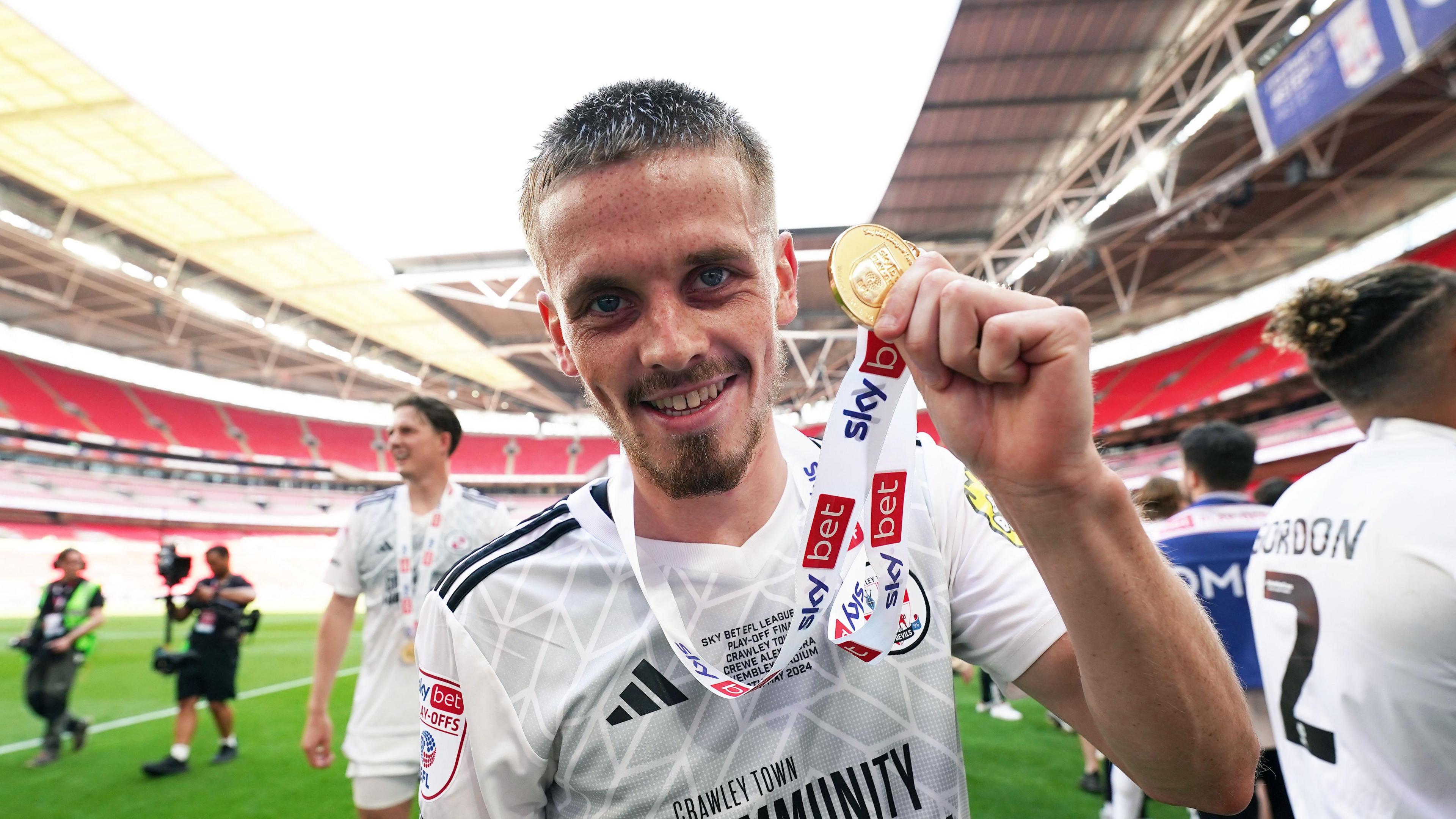 Ronan Darcy holds a promotion medal up to the camera on the Wembley pitch