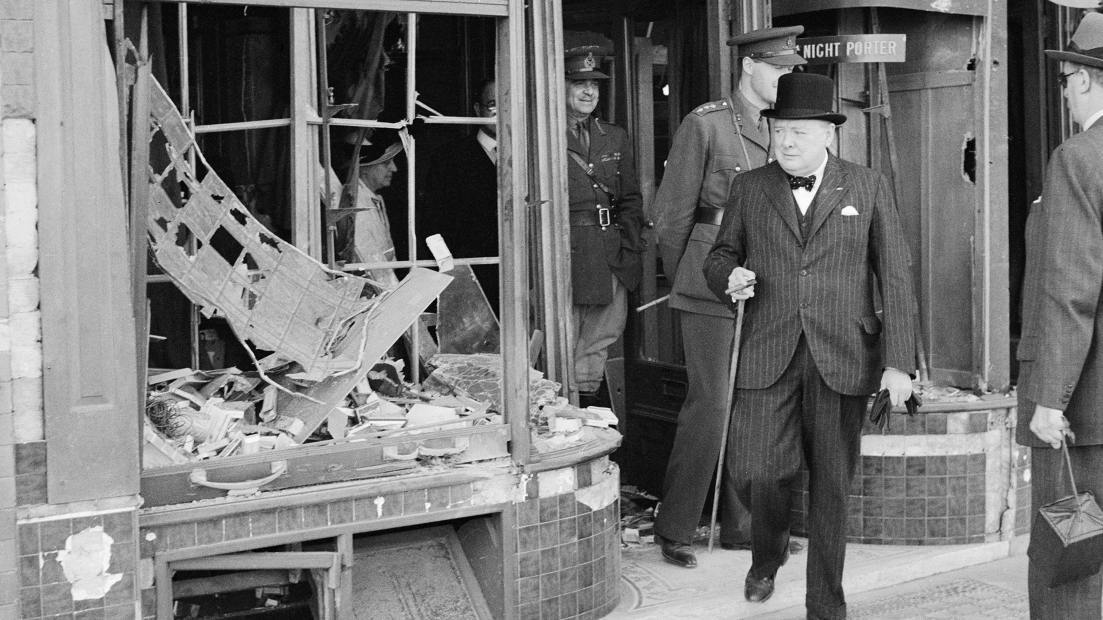 Black and white image of Winston Churchill wearing top hat and carrying cane outside a bombed out shop front in Ramsgate on 28 August 1940