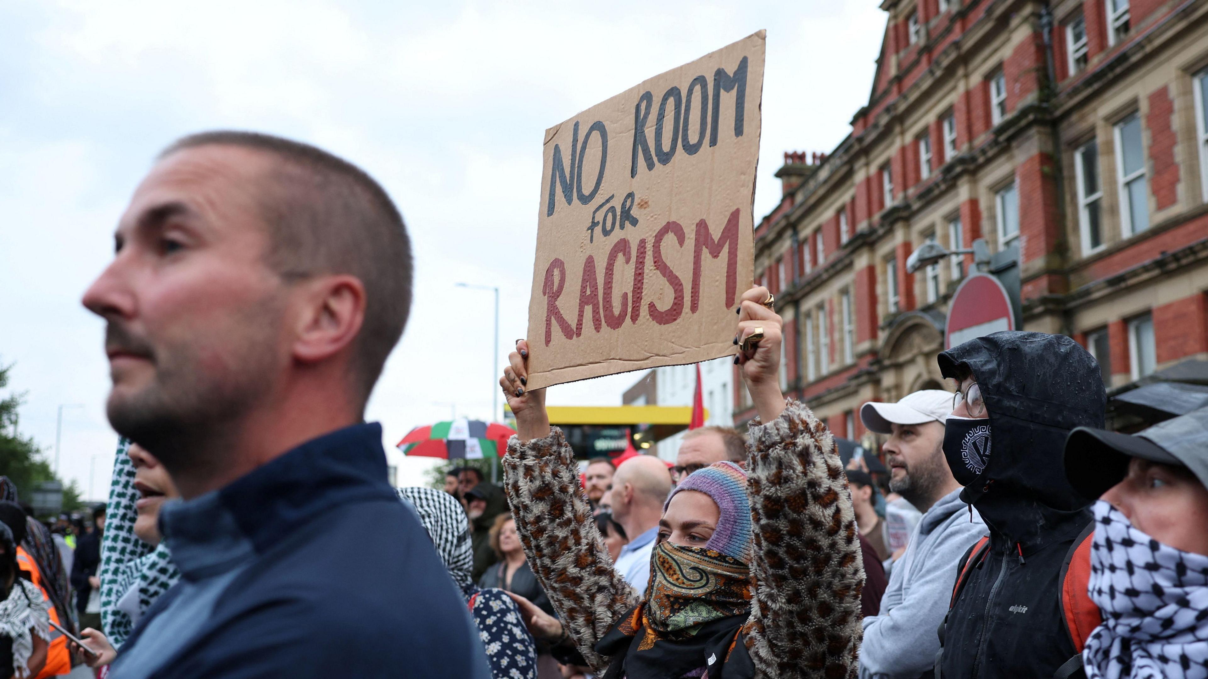 People outside the mosque in Liverpool, one woman holds a 'no room for racism' sign