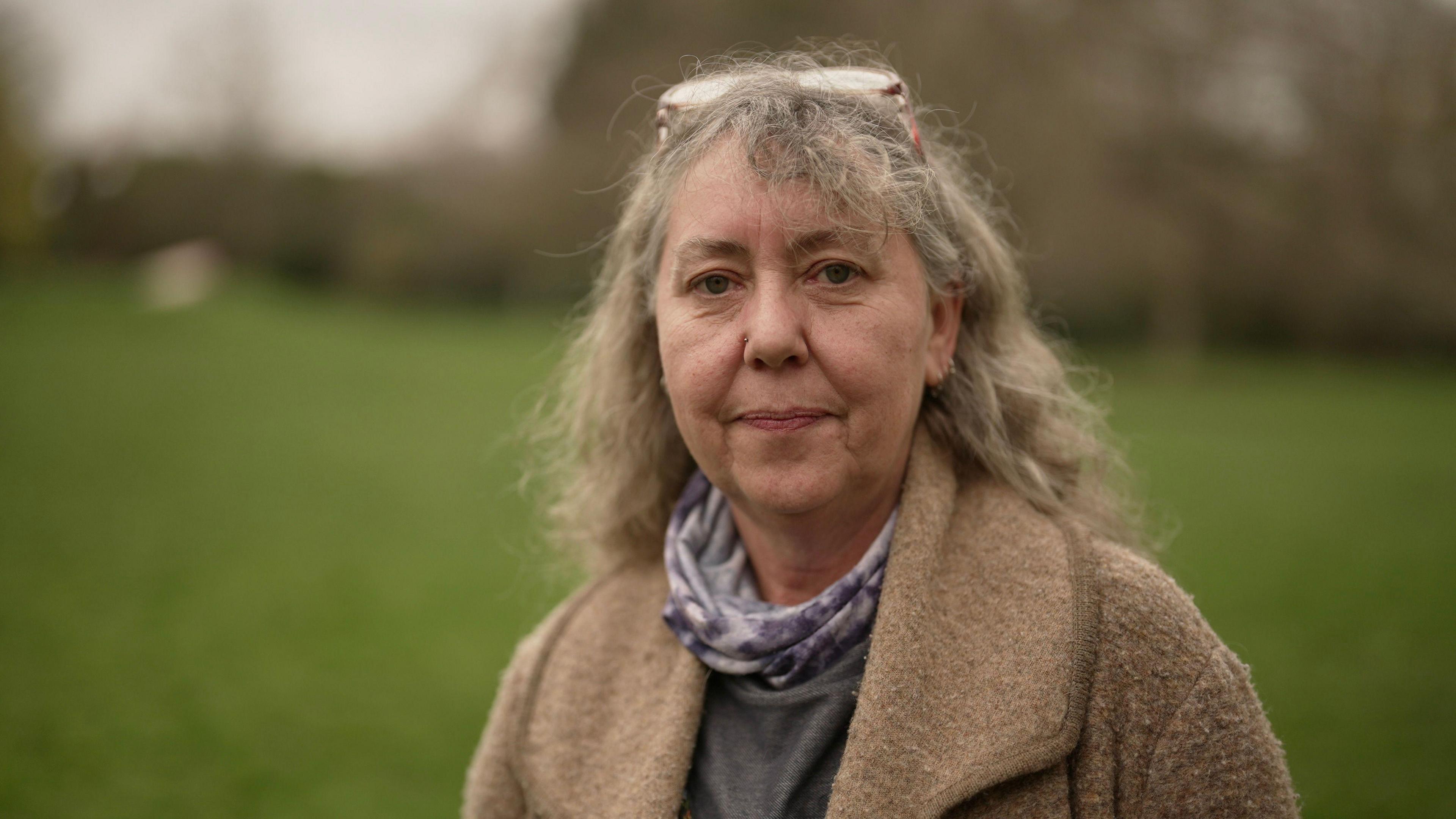Woman with grey hair and glasses on her hair smiles at the camera