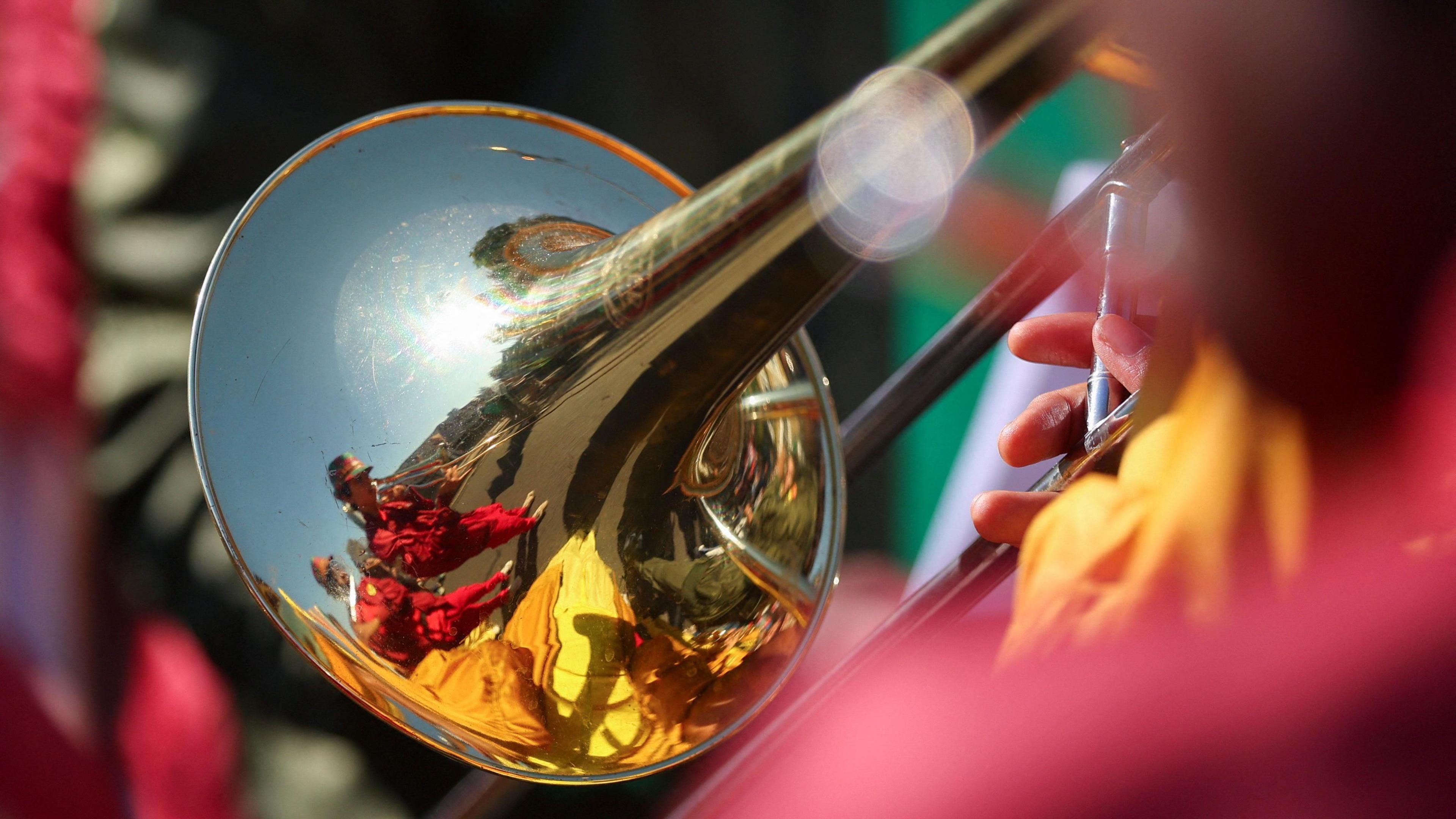 A musician wearing colourful clothes is reflected in the metal of their instrument.