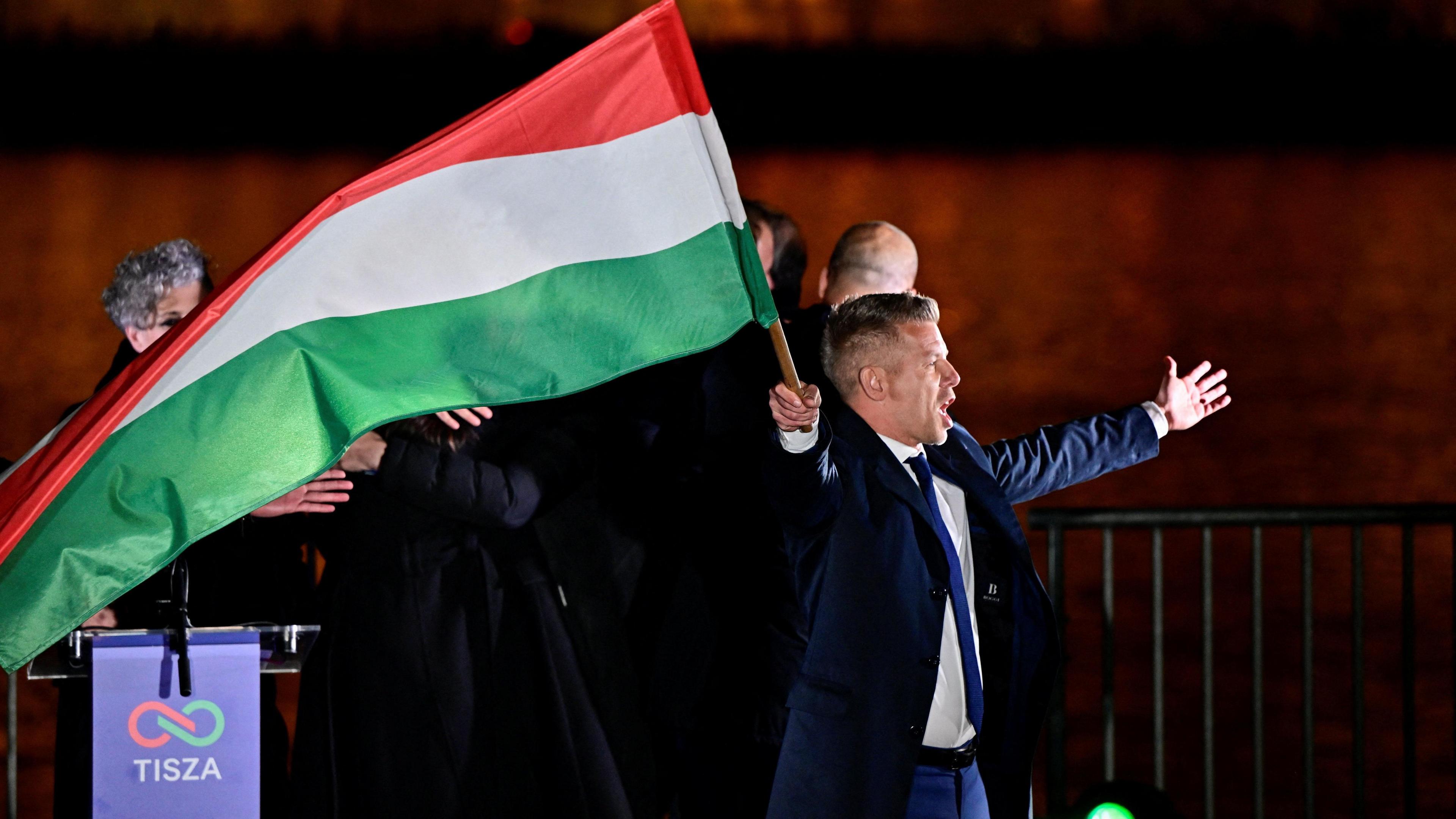 Peter Magyar waves a Hungarian flag with arms outstretched.