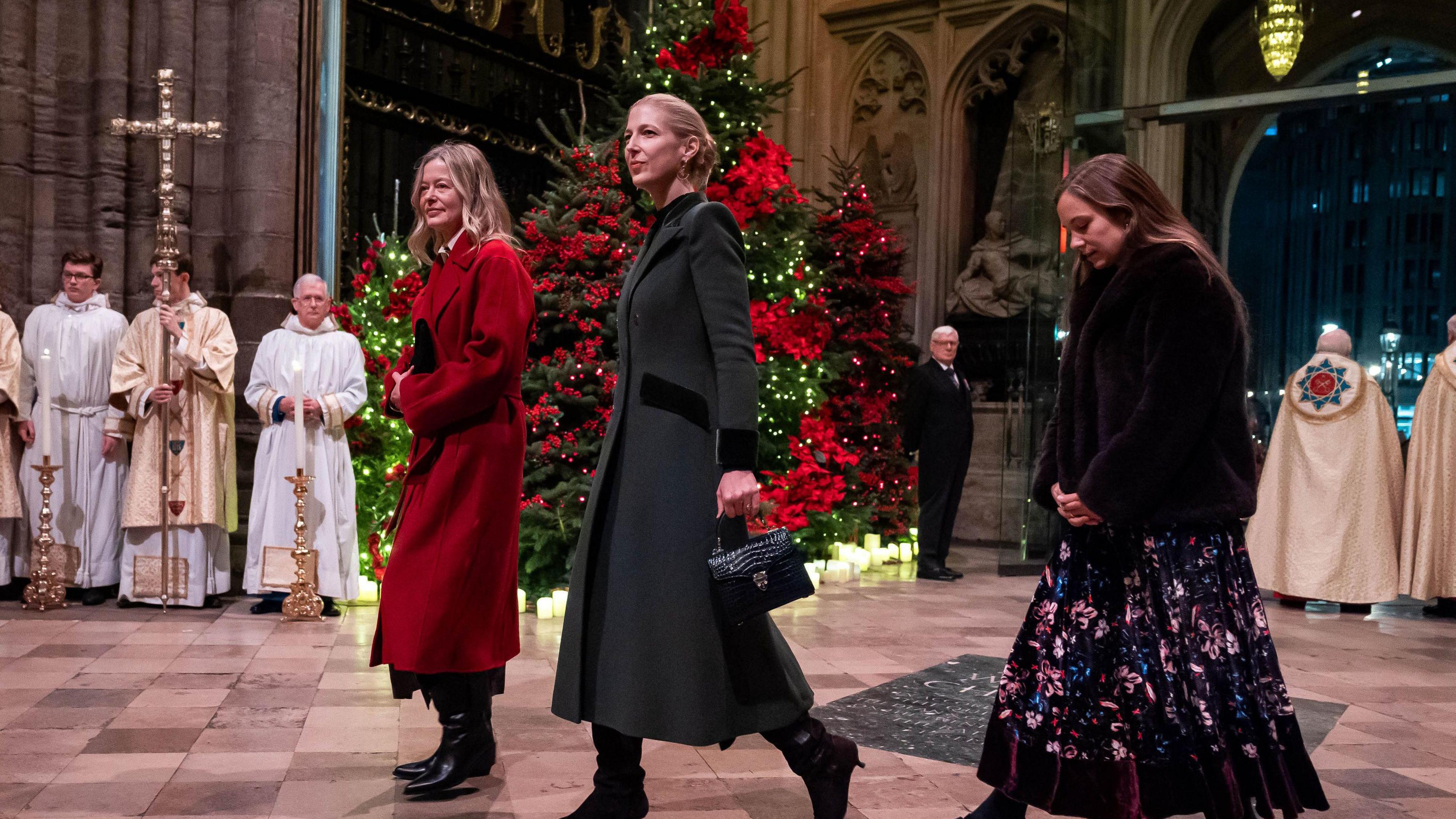 Lady Helen Taylor, Lady Gabriella Windsor and a third woman walk into Westminster Abbey with a Christmas tree and some priests stood behind them