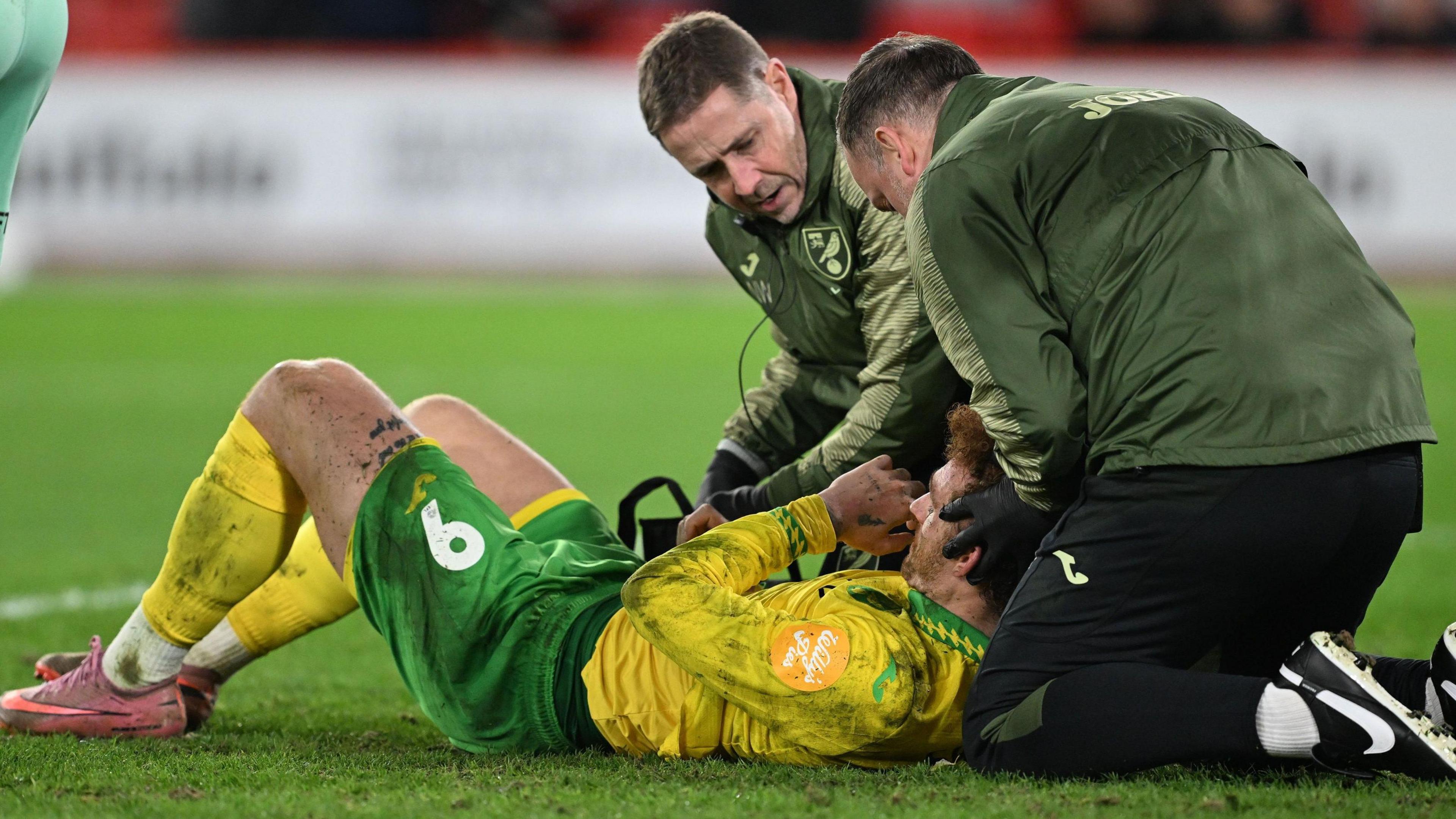 Josh Sargent, lying on the pitch, receives treatment from the Norwich City medical staff during their game with Sheffield United