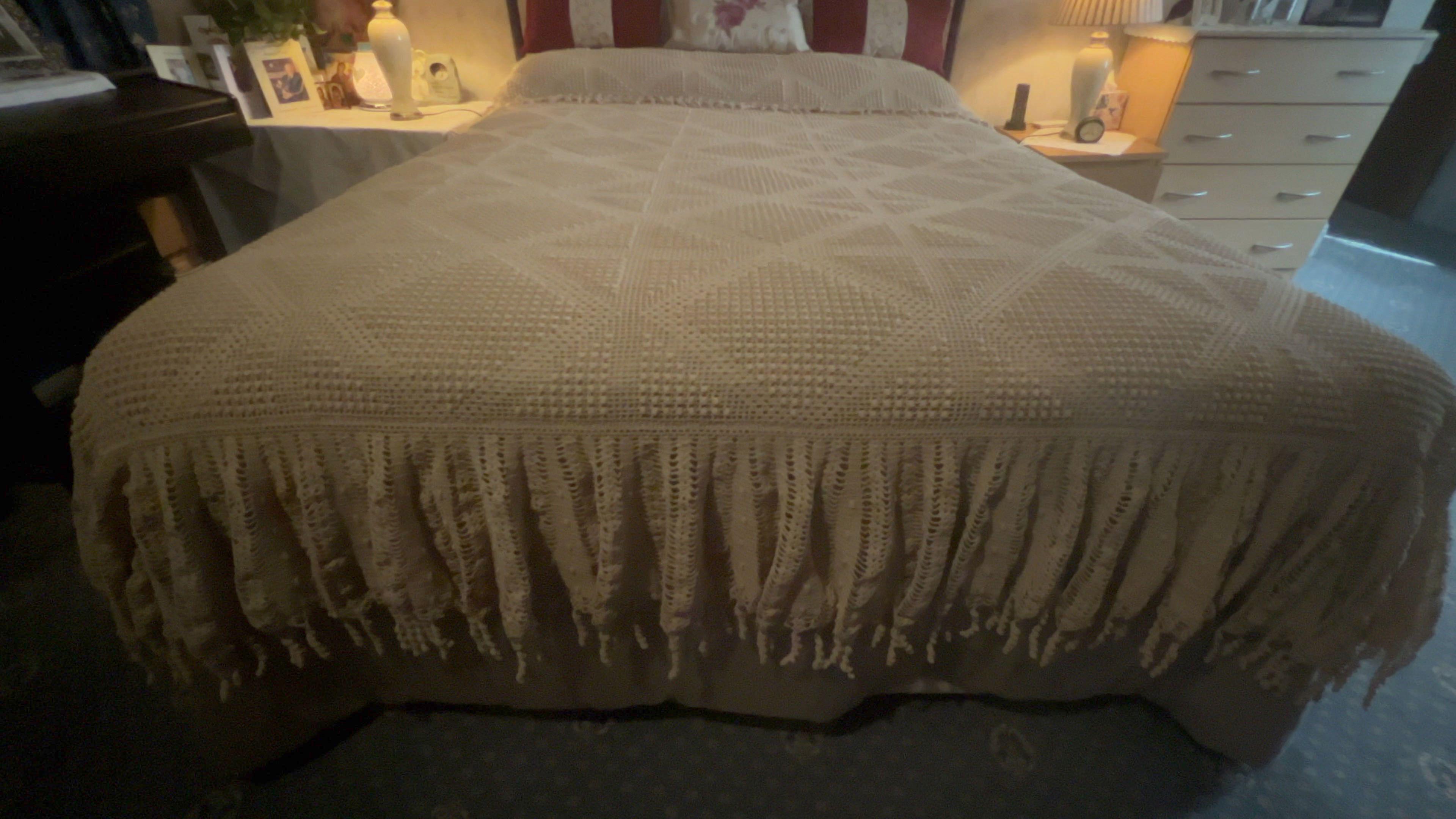 A photo of a beige crocheted bedspread which lies neatly on top of a double bed in a bedroom.
