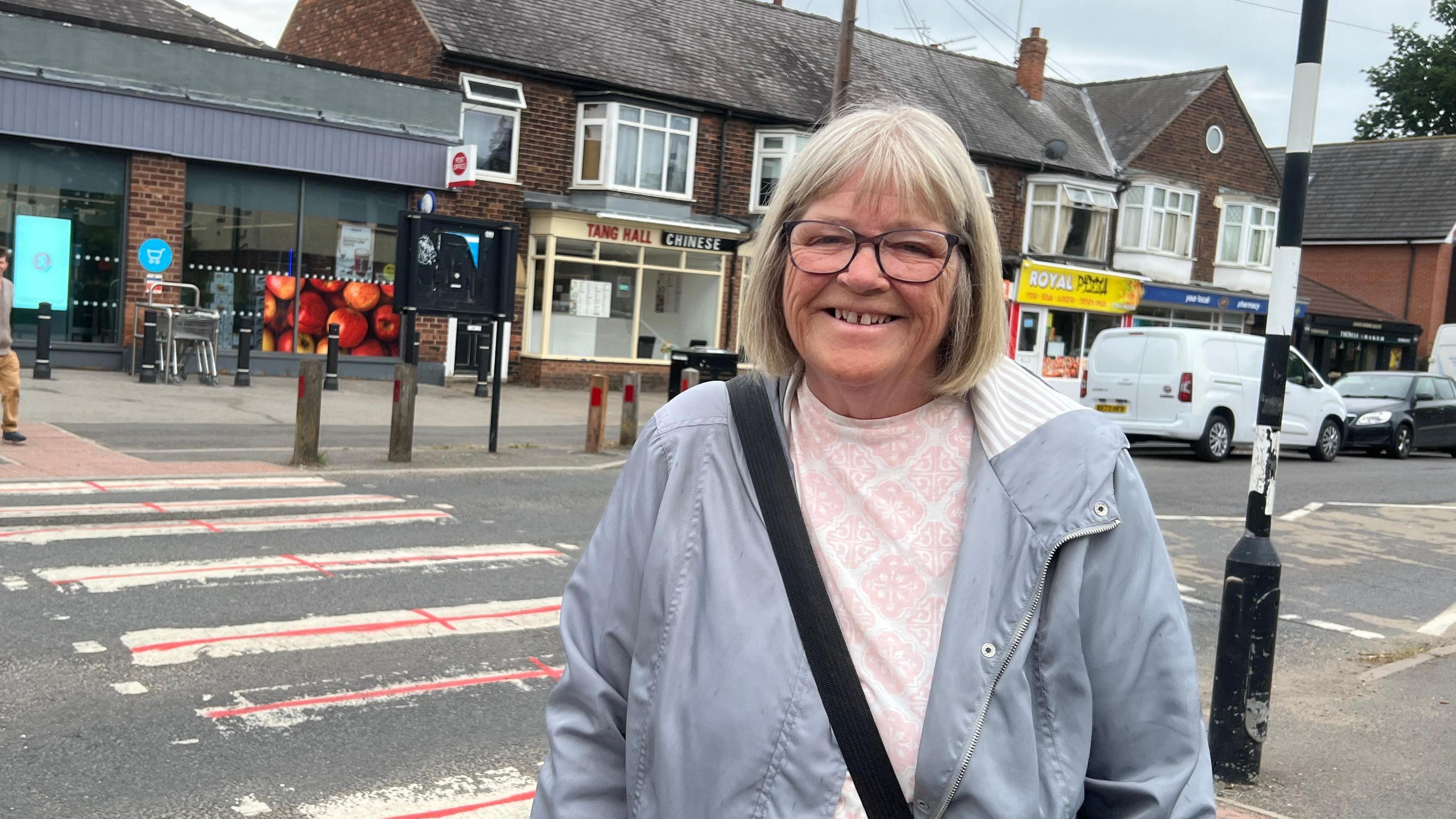 Patricia Pallister is standing in front of a zebra crossing. It has been painted to make it appear like a row of St George Cross flags.