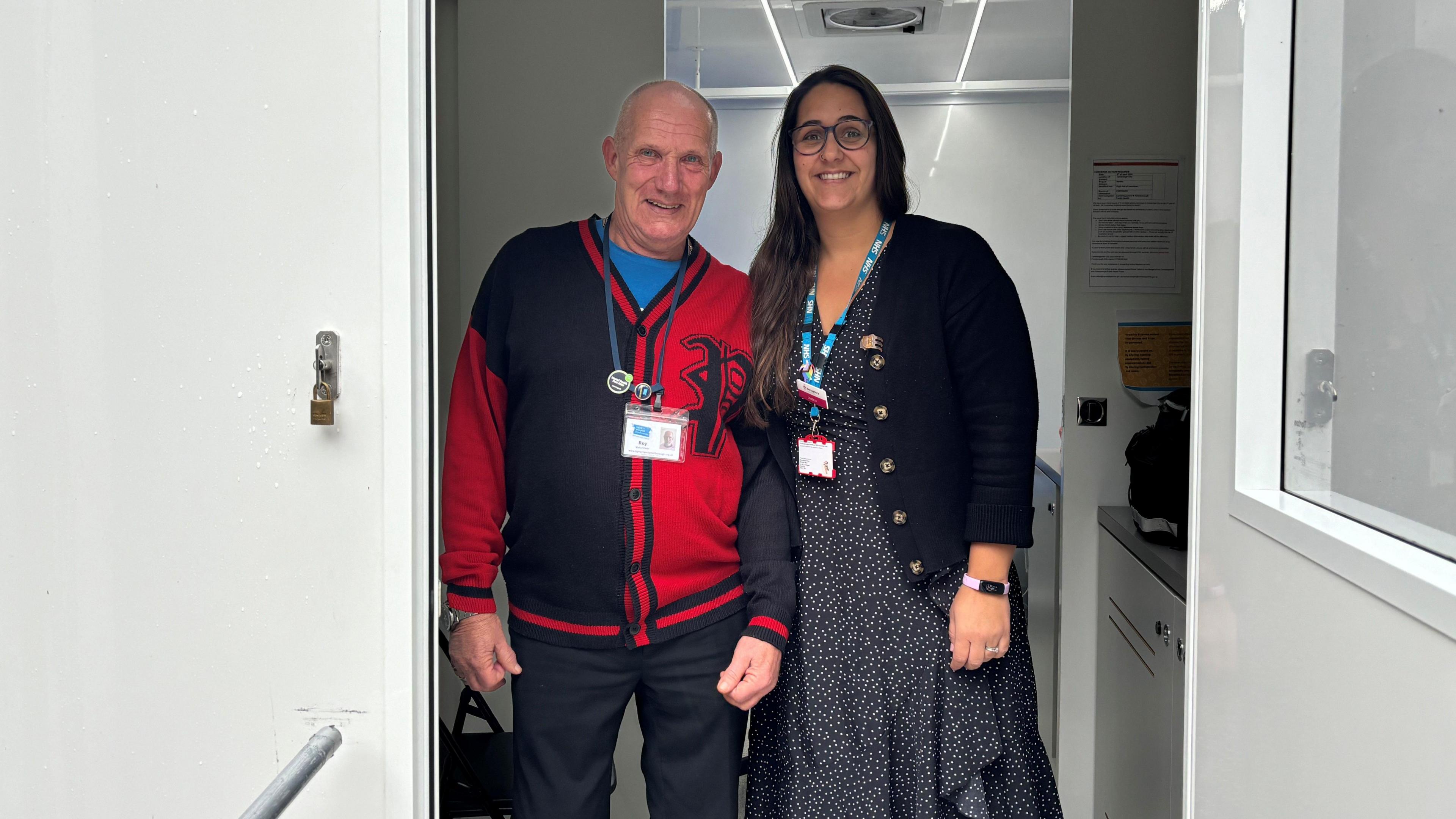 Roy wearing a black and red cardigan standing next to Jess wearing a black and white spotted dress and a black cardigan 