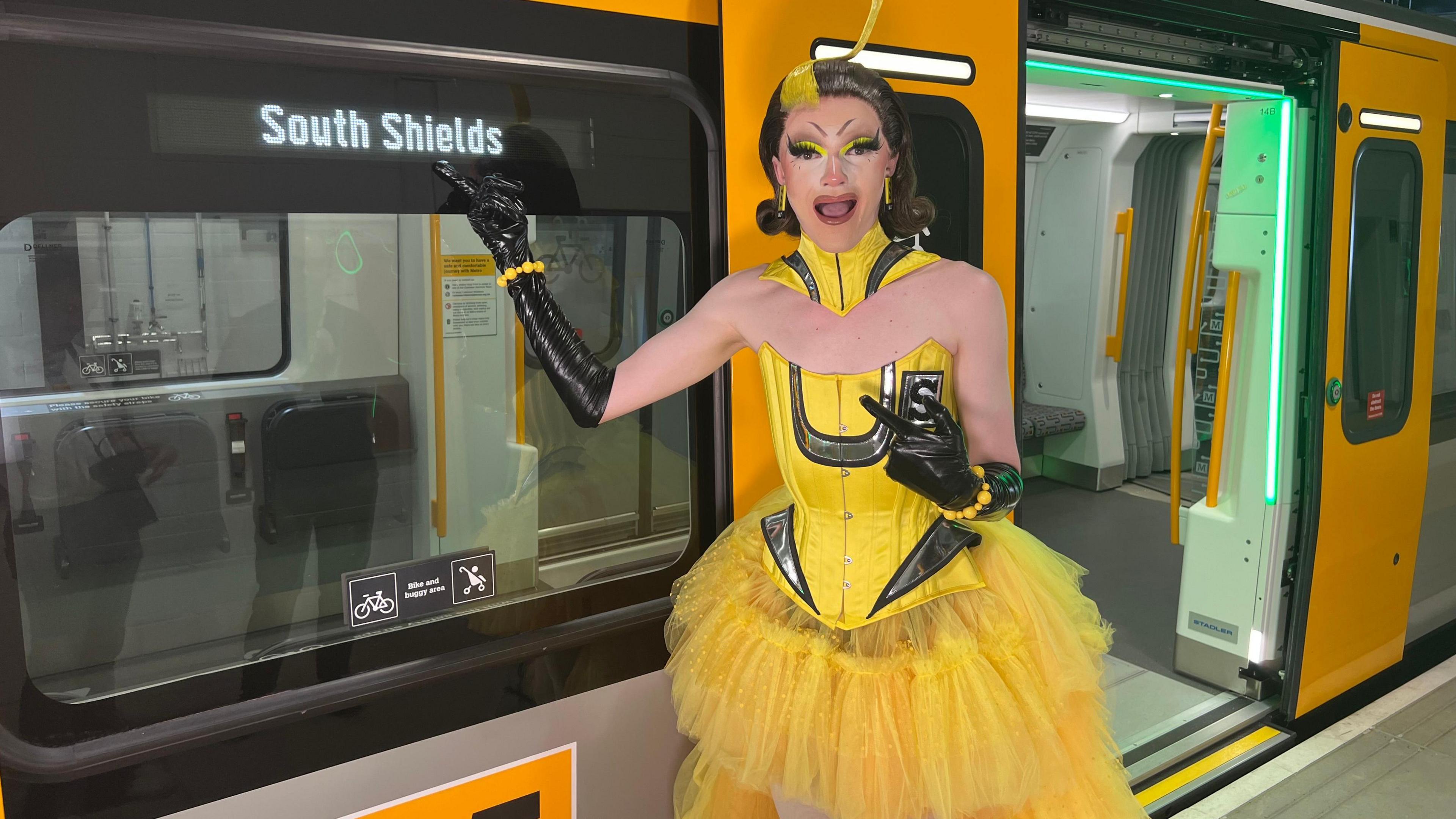 Sally TM pointing at the destination on the side of the grey and yellow Metro, which is South Shields. She has a shocked look on her face.