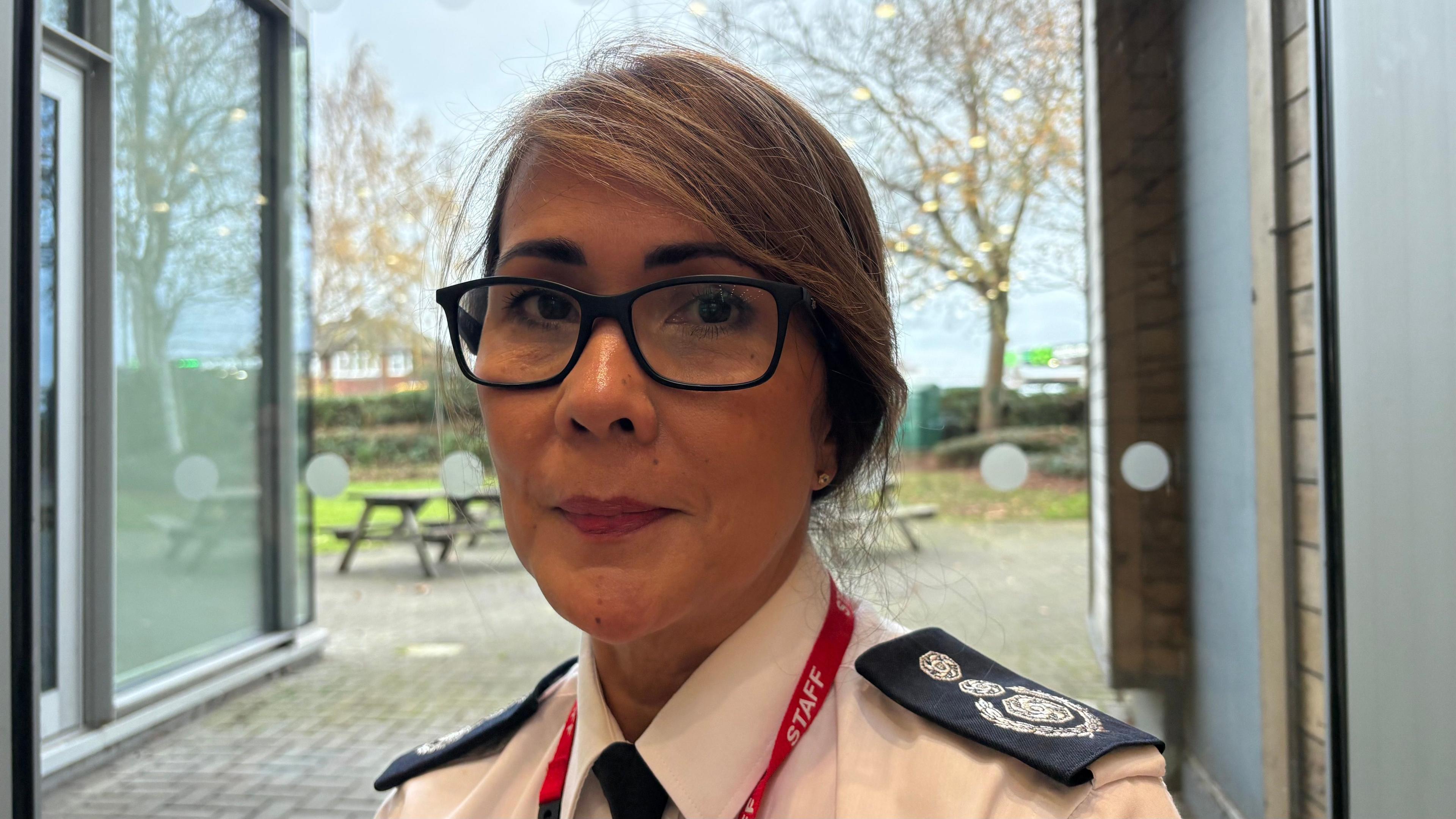 Louise Harrison, with medium-length brown hair tied back, dark-rimmed glasses, looking at the camera and wearing a white fire service shirt with the crest on each shoulder, a black tie and red lanyard