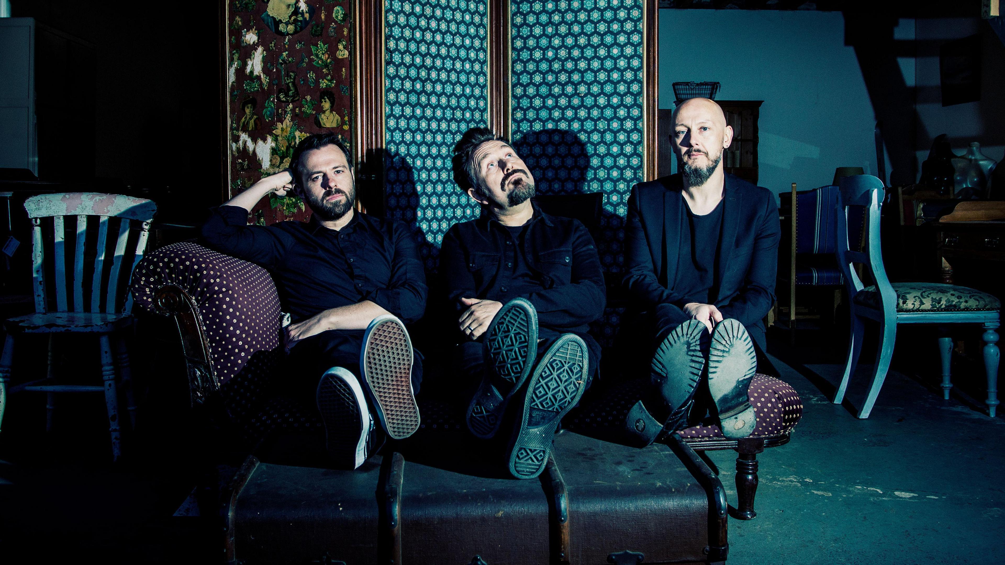 Members of the bank Therapy? photographed sitting on sofa with their feet up on a box