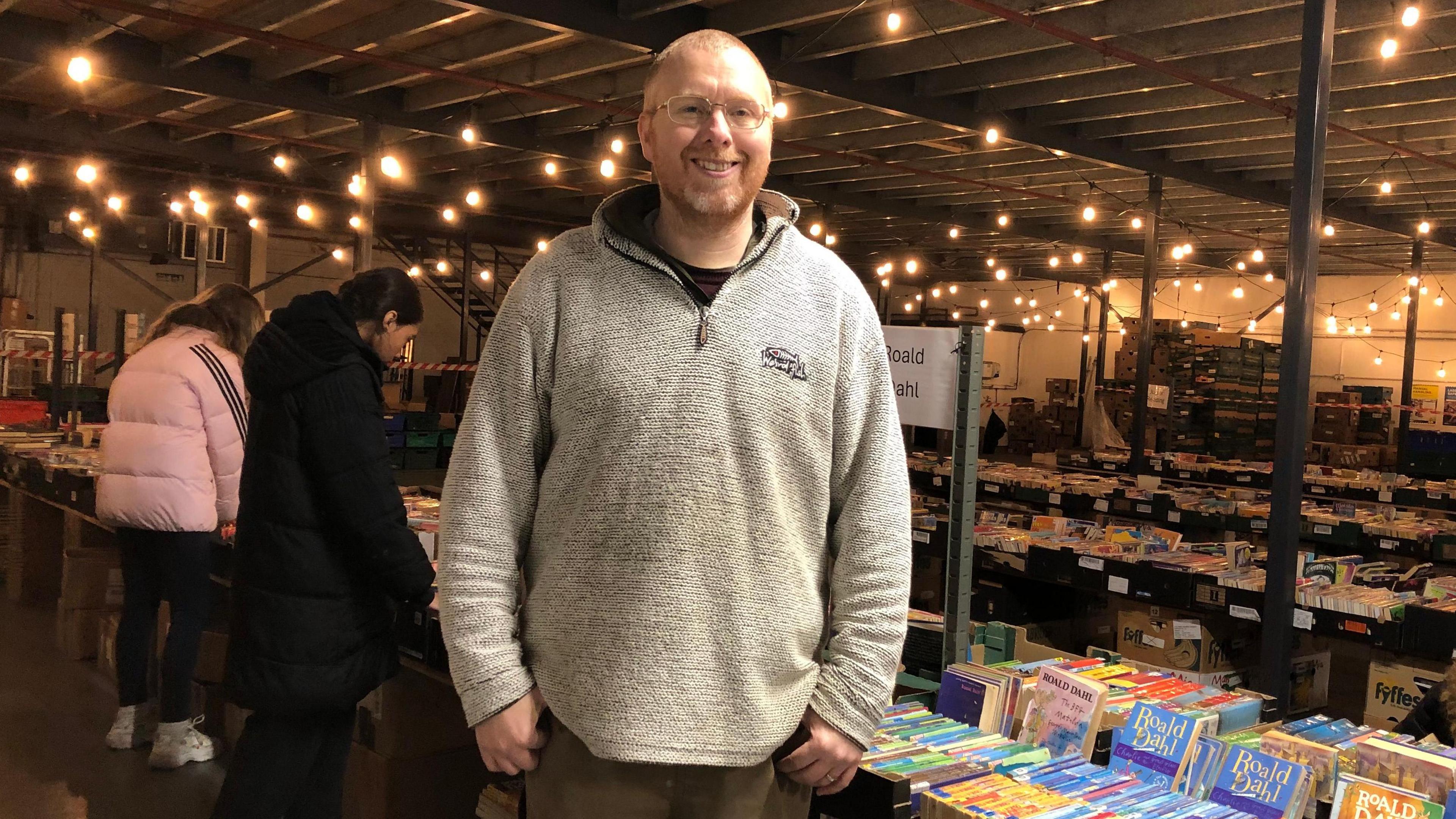 Second-hand bookseller Stephen White stood in front of a table with books on it with children behind looking at books