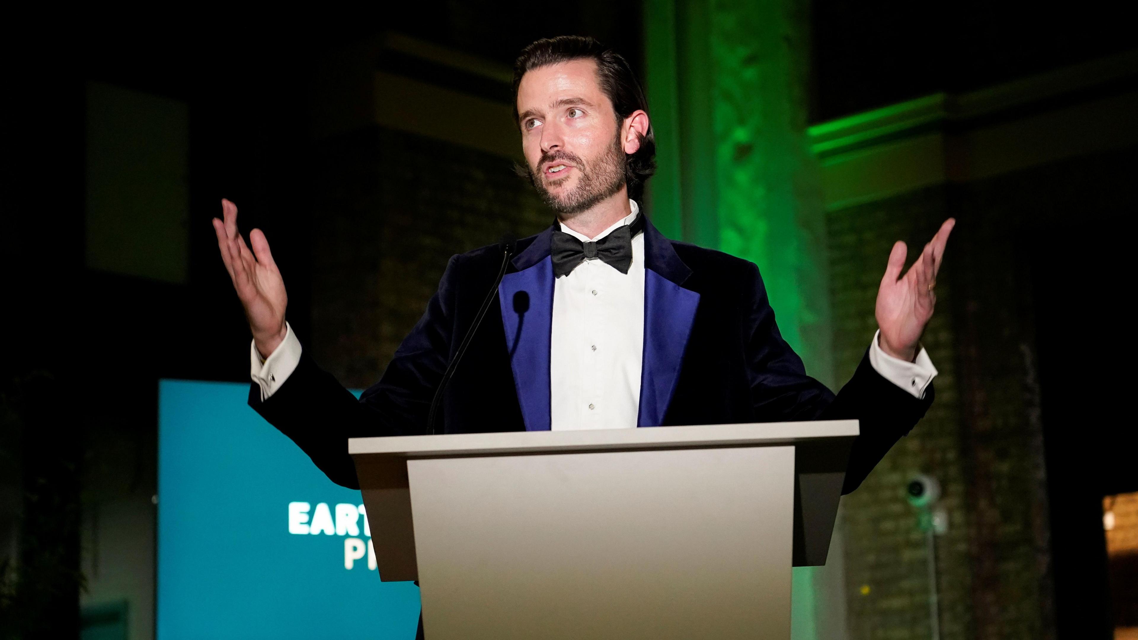 Jason Knauf dressed in formal black tie, delivering a key note speech at an Earthshot Prize event.