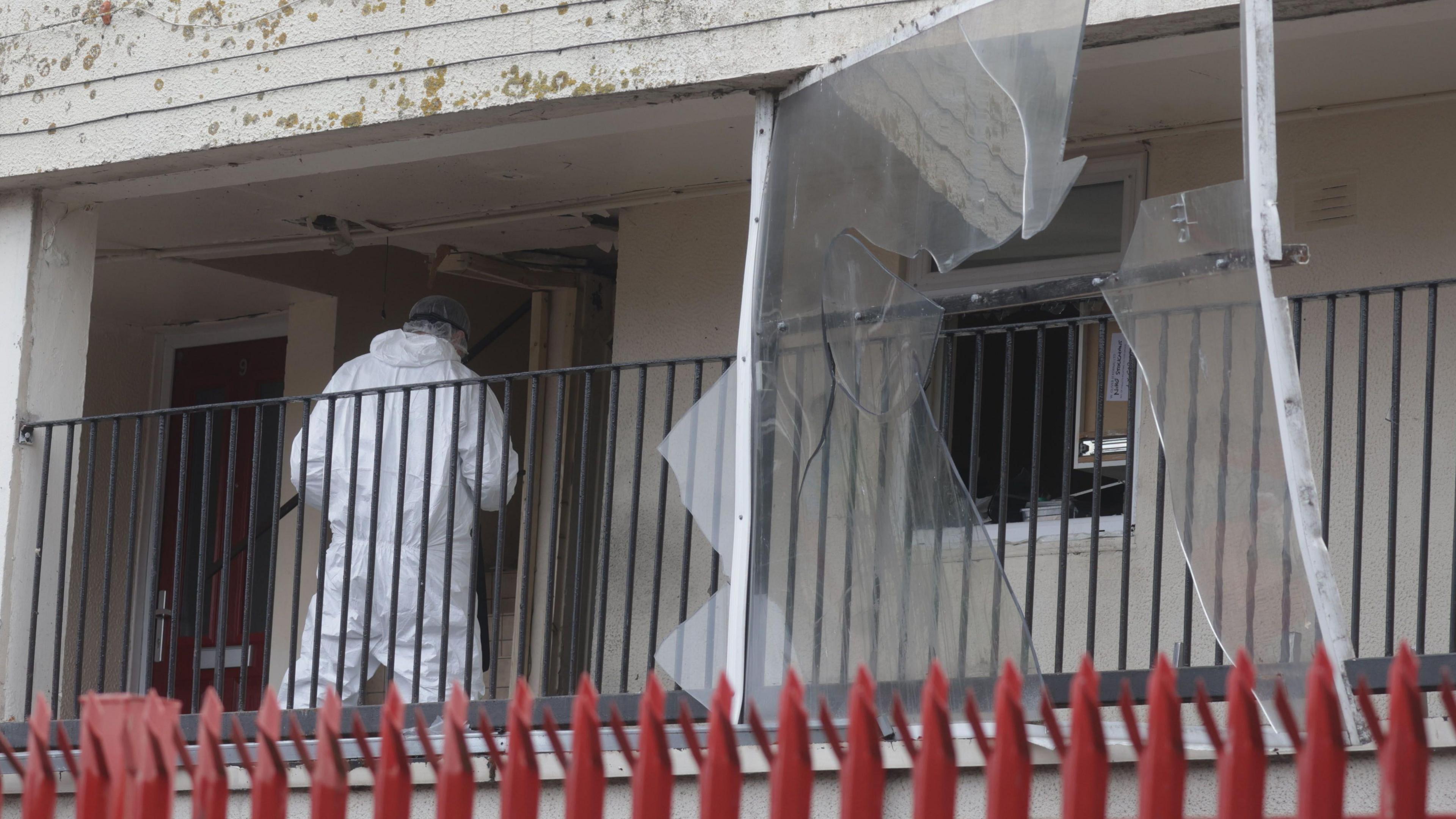 A person in a forensic suit entering a flat. Red railings are at the bottom.