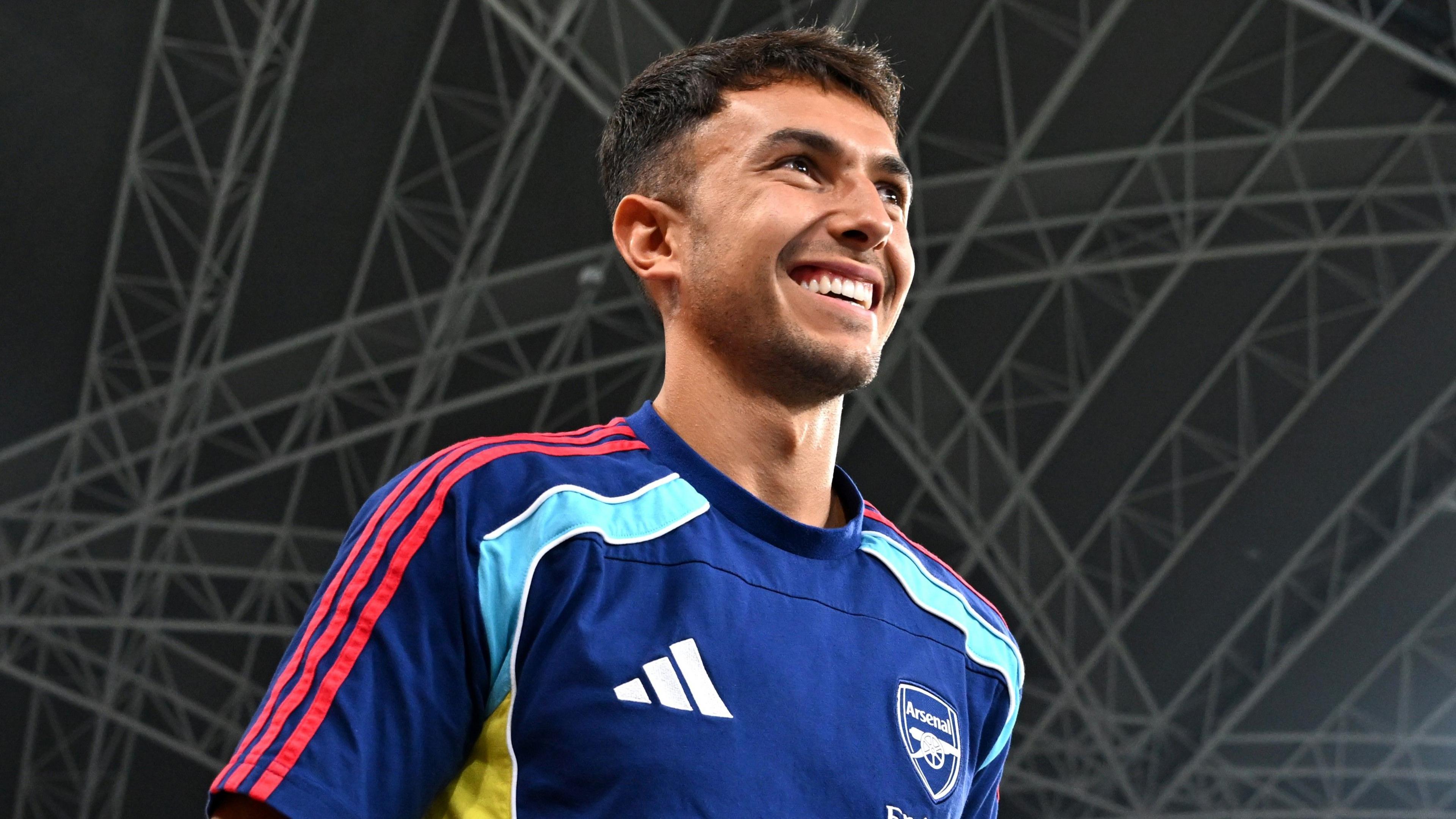 A smiling Martin Zubimendi looks into the distance pre-season game, wearing an Arsenal training top