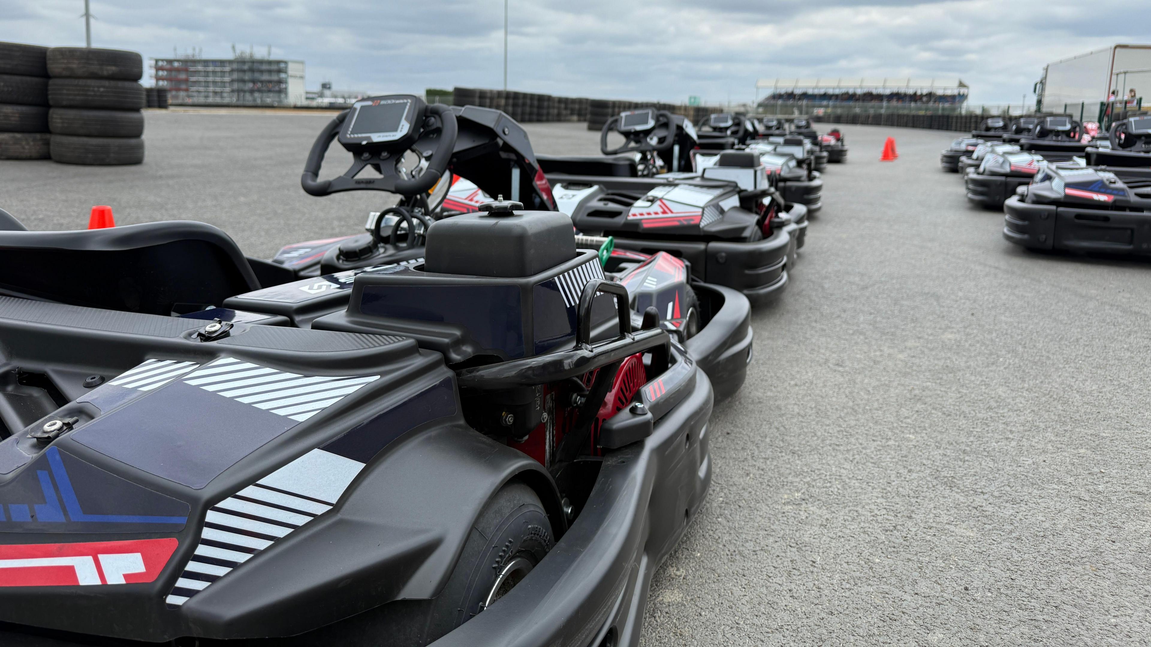 A close up of a black go kart with red and white markings on it. There are about 10 more lined up in the background.