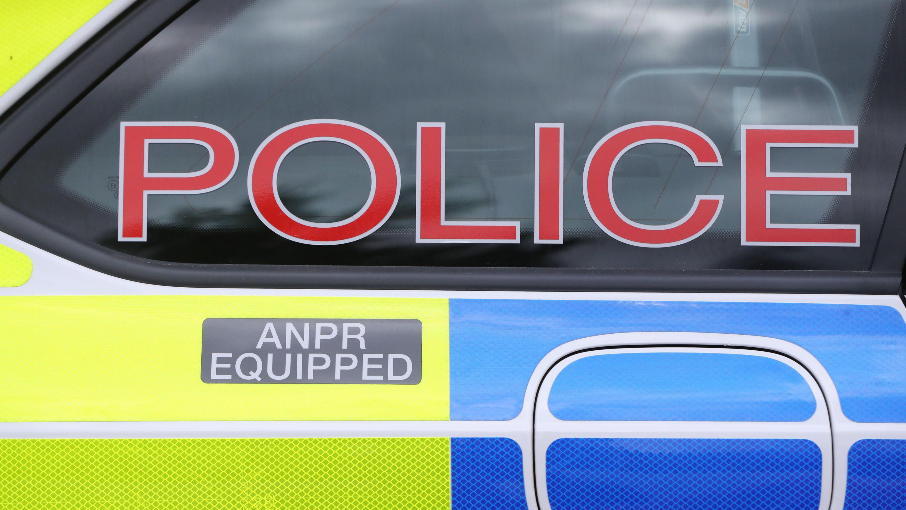 A yellow, blue and white police car with 'police' written in red letters on the blacked out window.