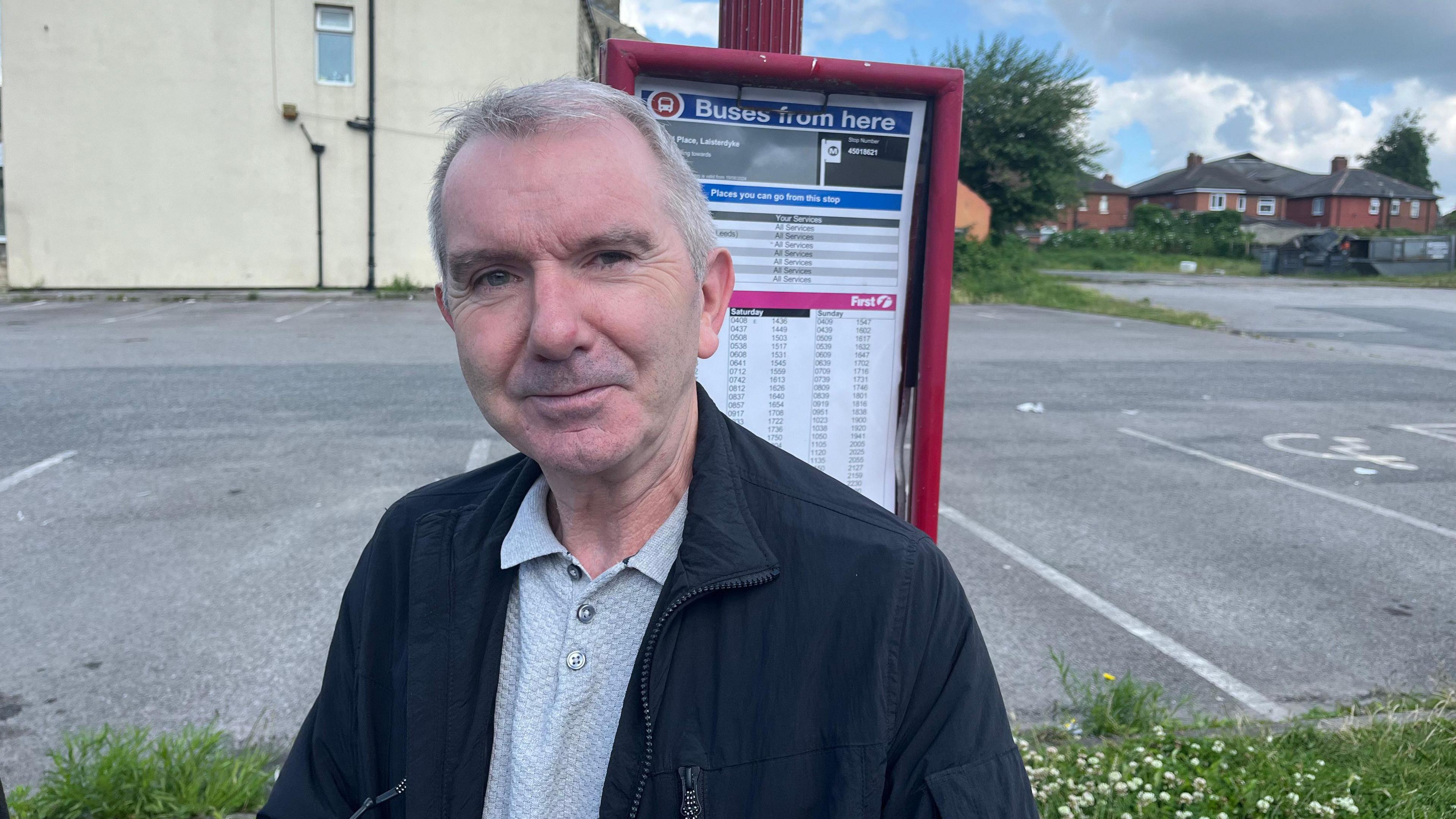 David Hardwick standing in front of bus stop with timetable