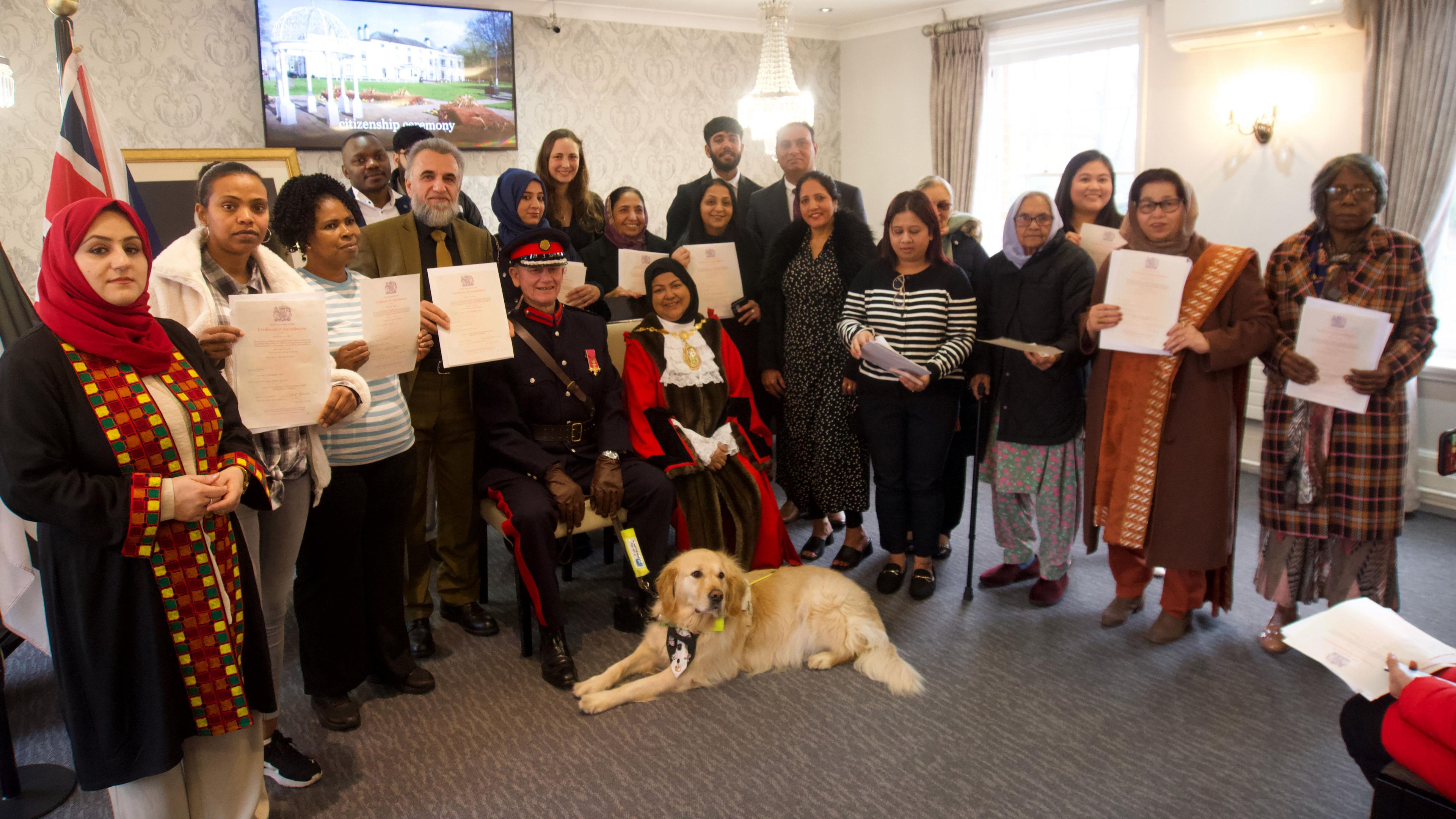 A group of 21 people at a UK citizenship ceremony. Nineteen have their certificates and seated are a deputy lieutenant in military uniform and the female mayor of Sandwell.