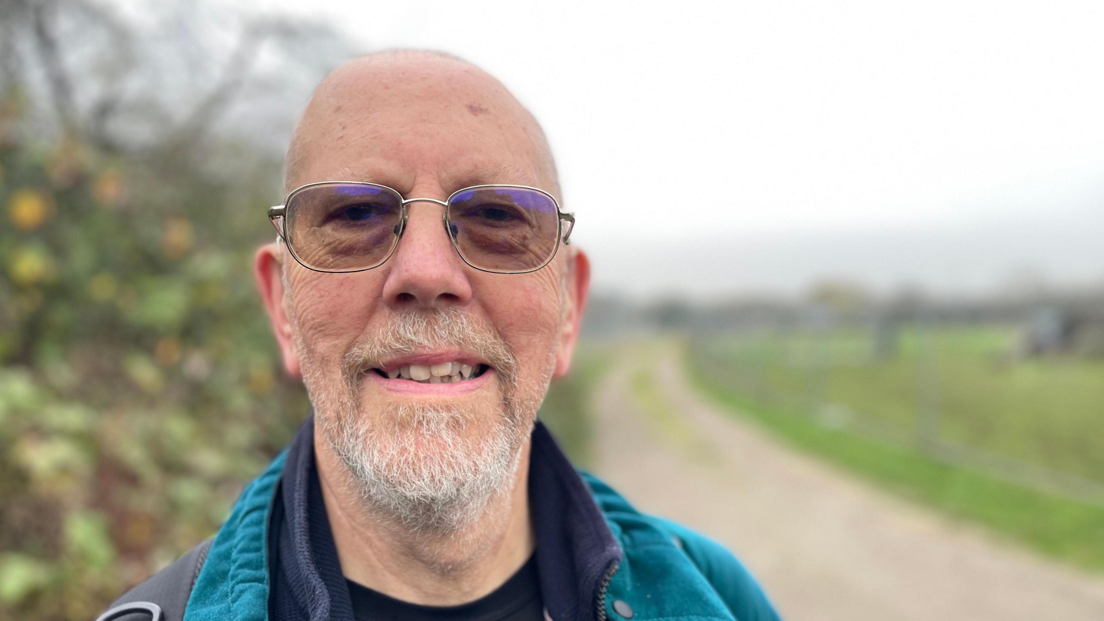 Bearded man with glasses in the countryside in front of a footpath 