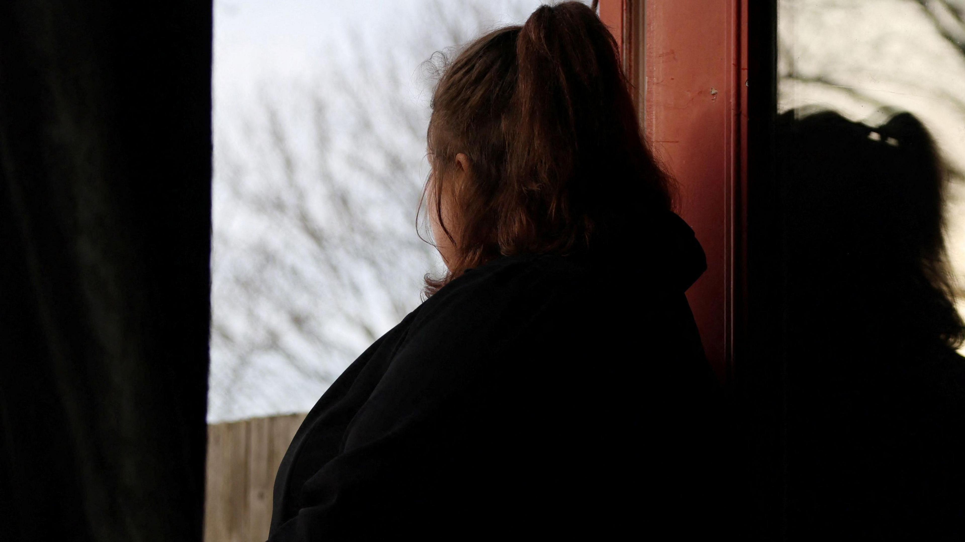 A former grooming gang victim poses with her fae obscured as she looks out a window