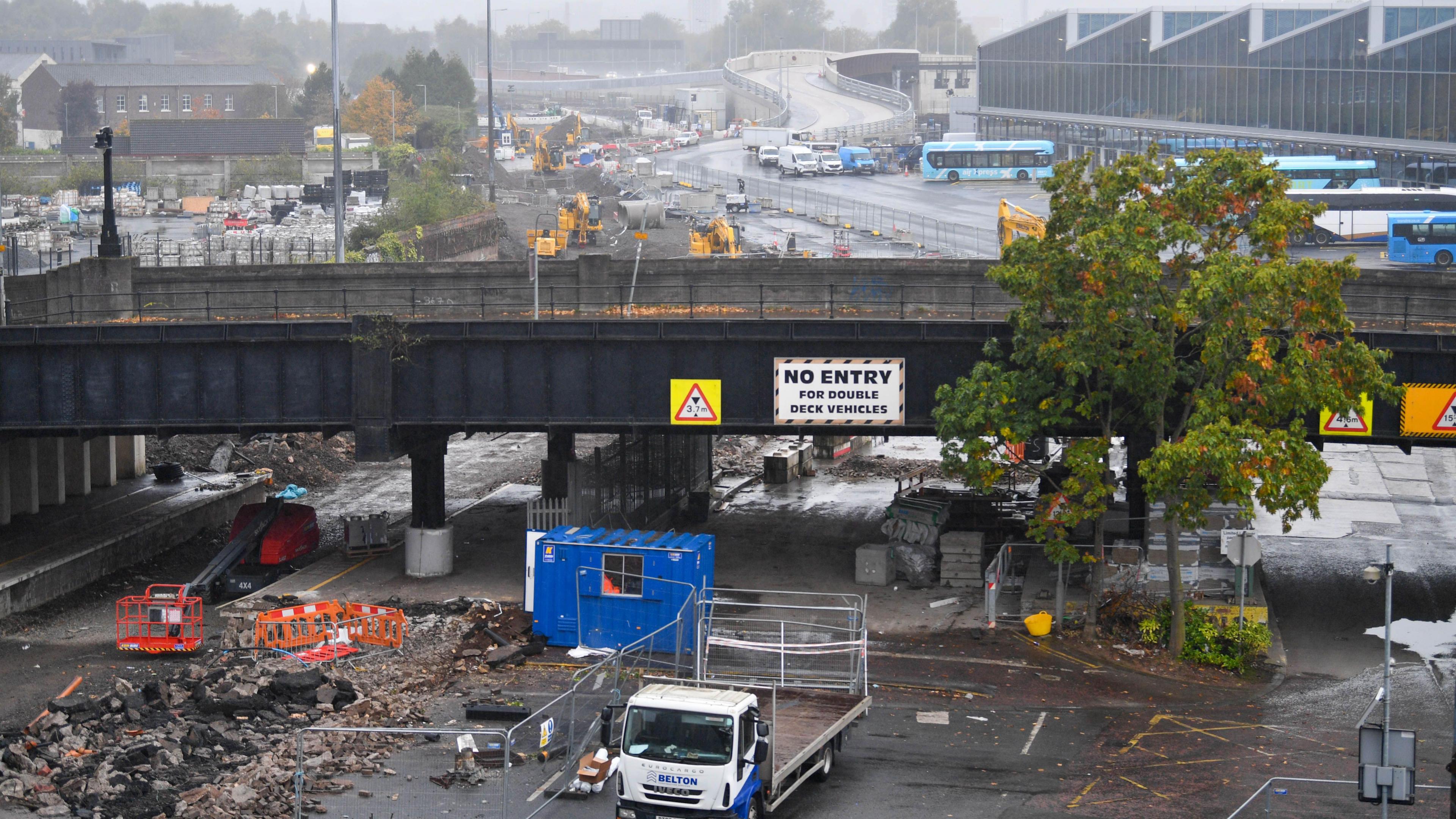 Side view of Boyne Bridge. Bricks and rubble lie underneath. A lorry and portacabin are also underneath. The new Grand Central Station and buses can be seen in the background.