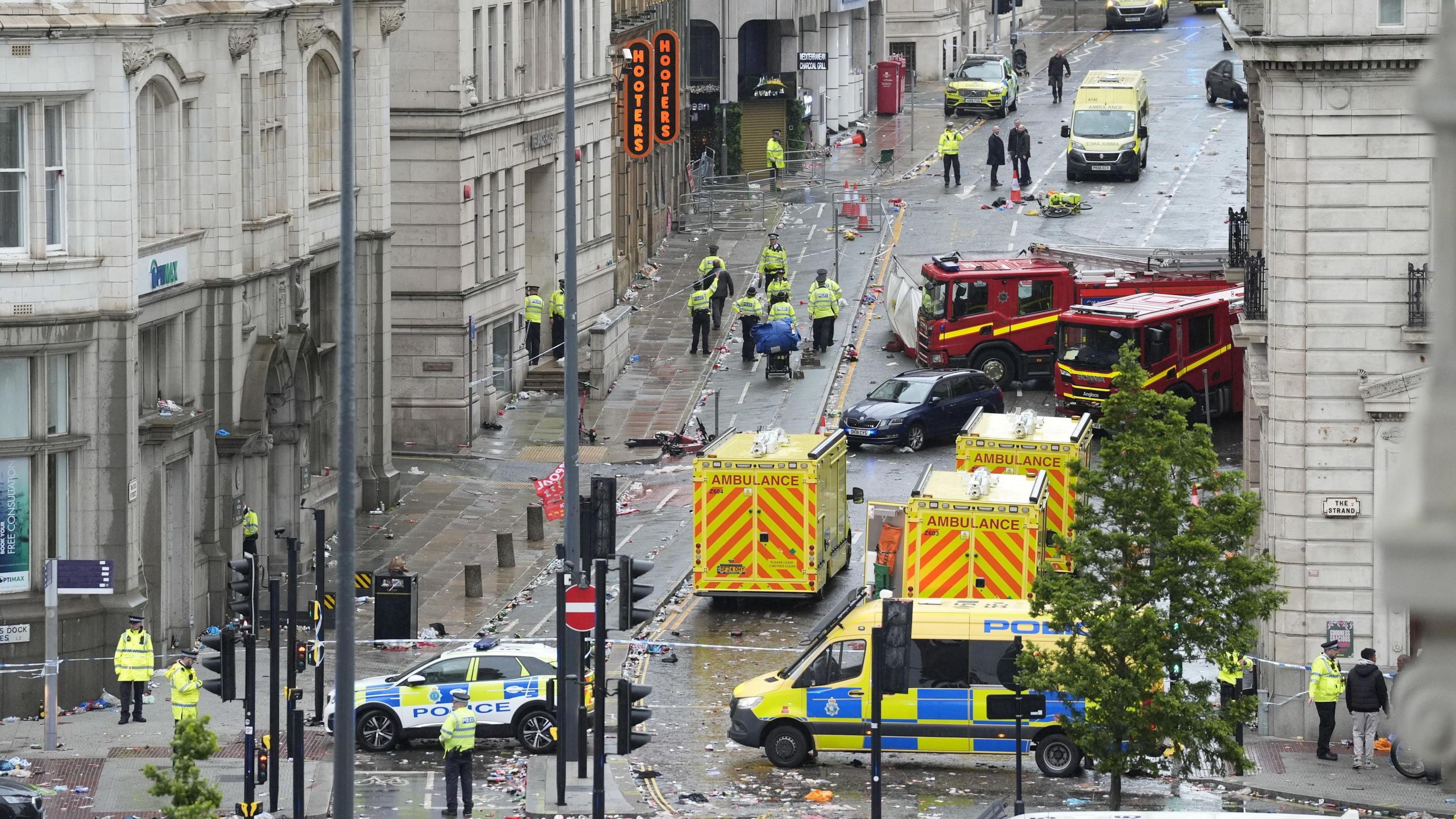 Fire engines, ambulances, police cars and groups of police officers can be seen from behind a police cordon.
