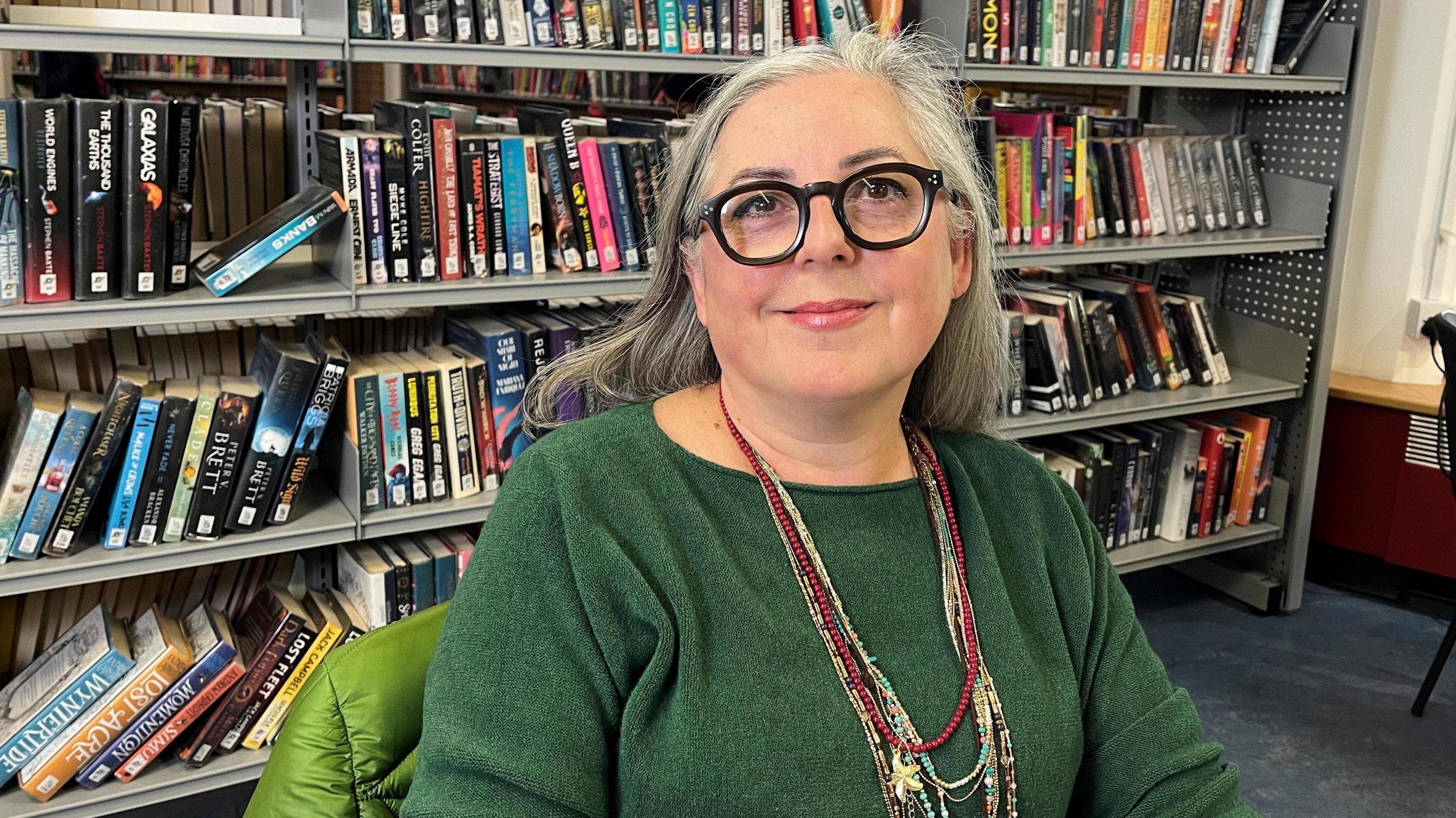Library visitor Lola Stanley looking at the camera. She is sitting in front of a shelf of books in Chipping Barnet Library