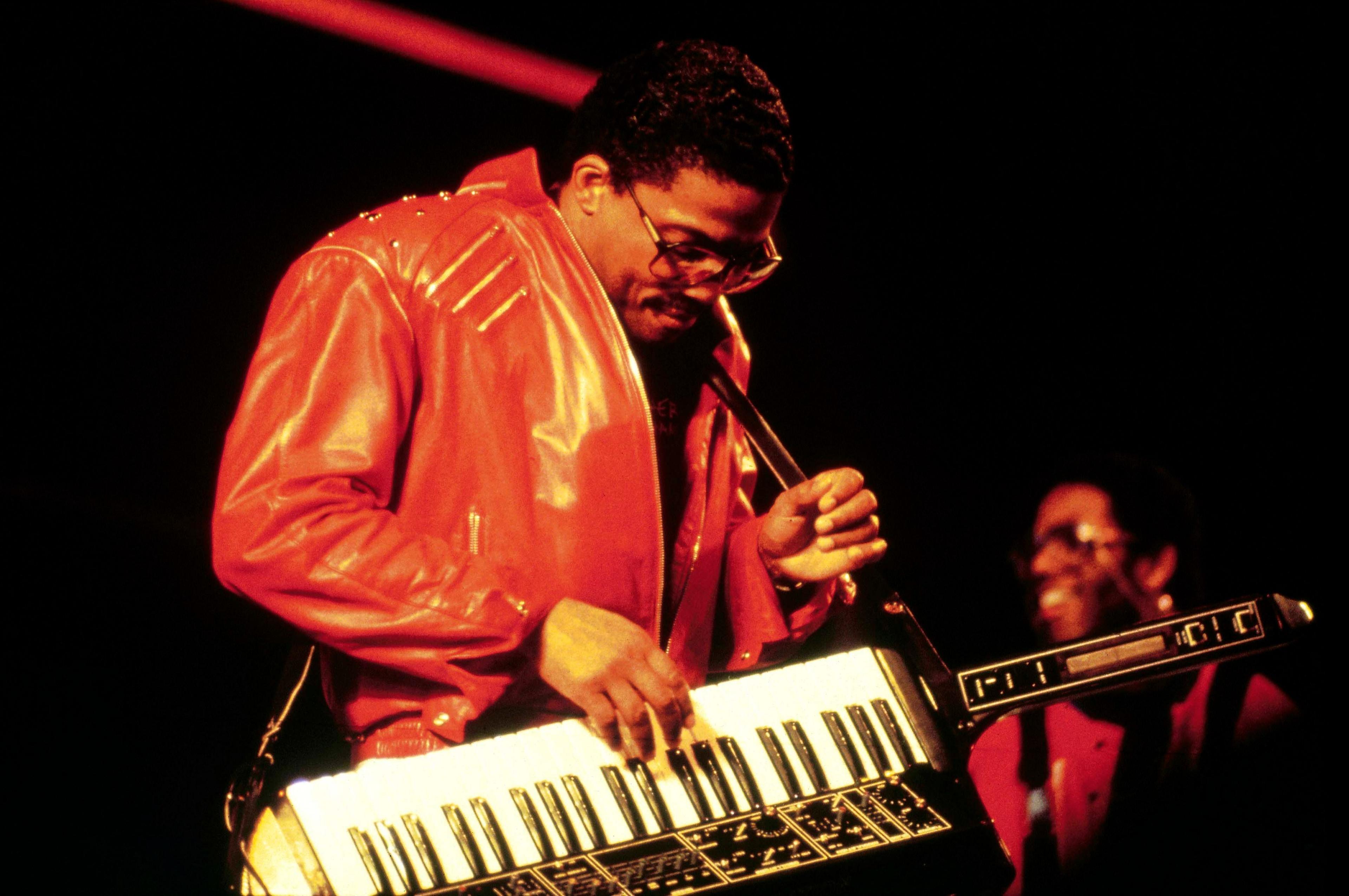 Herbie Hancock playing a keytar whilst wearing an oversized red leather jacket.