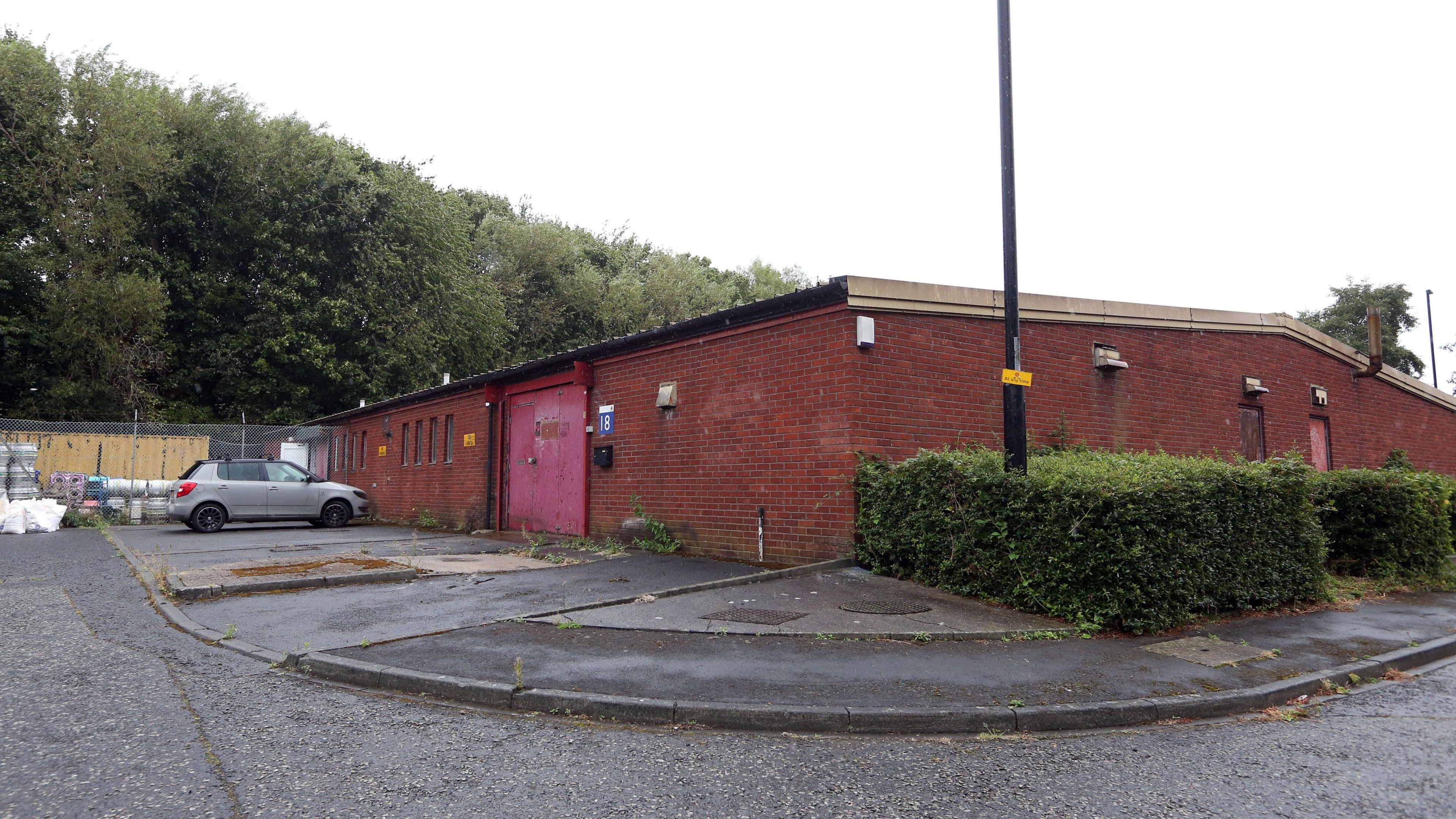 A one-storey brick building with a silver car parked outside.