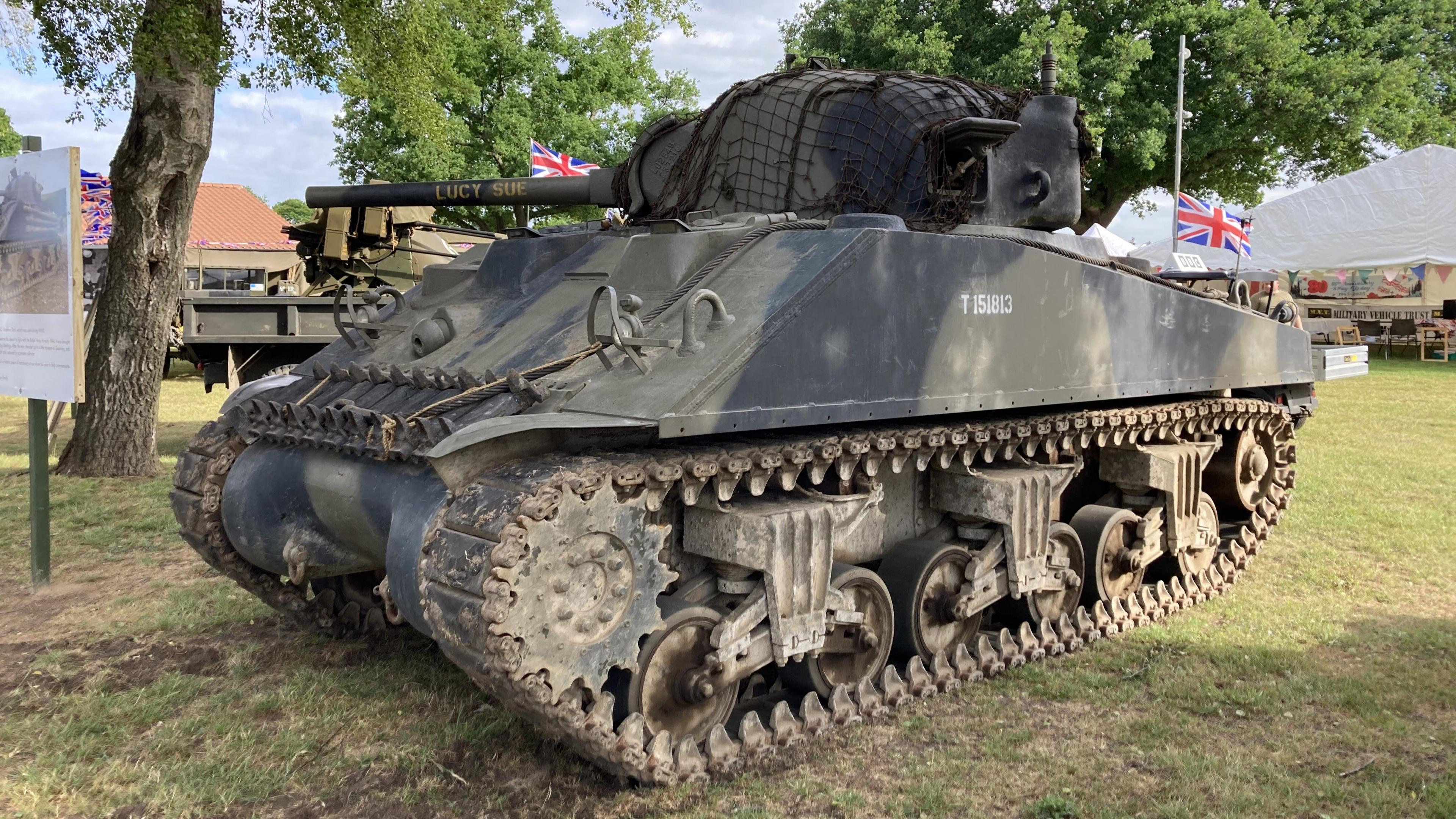 A Sherman tank rests in a grass field at the Suffolk Show. It is a camouflage colour.