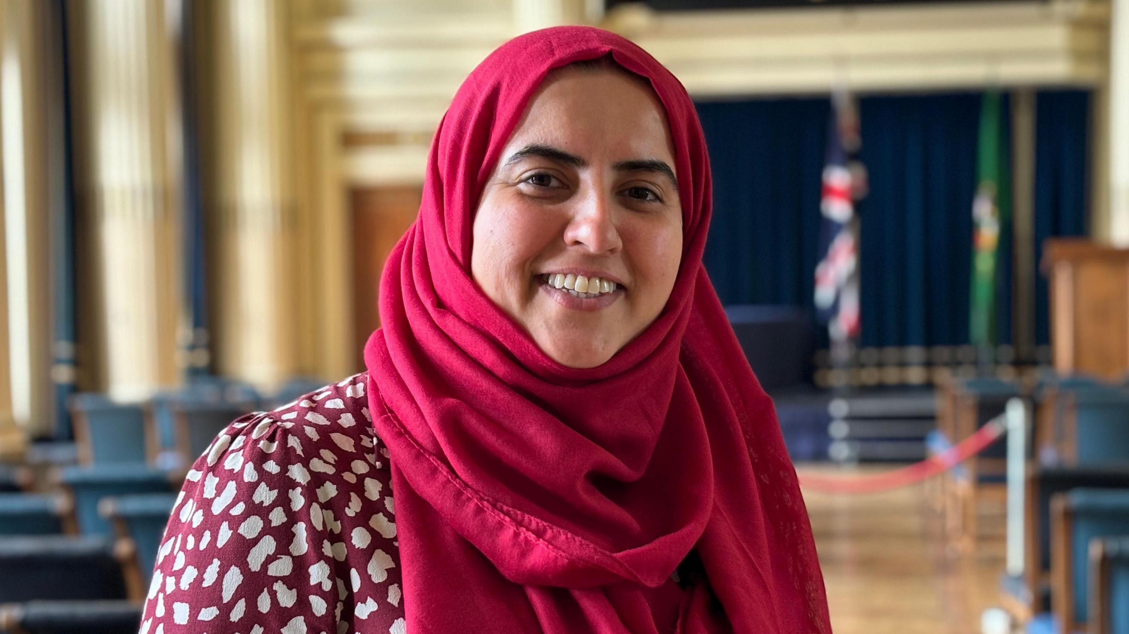 A profile shot of council leader Neghat Khan wearing a red headscarf and red top with white spots. 