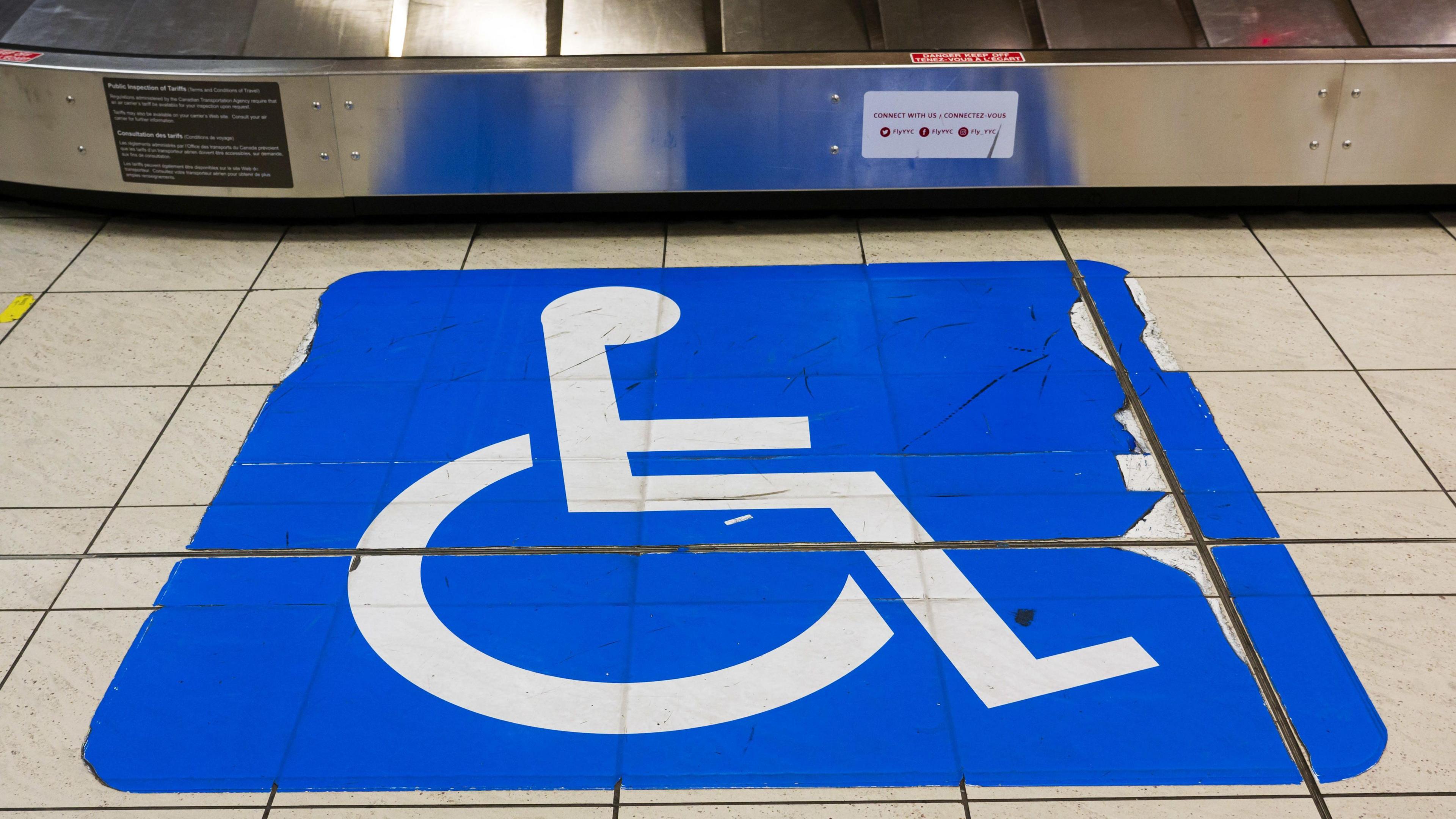 A sticker showing a wheelchair on the tiled floor next to a luggage reclaim carousel at an airport