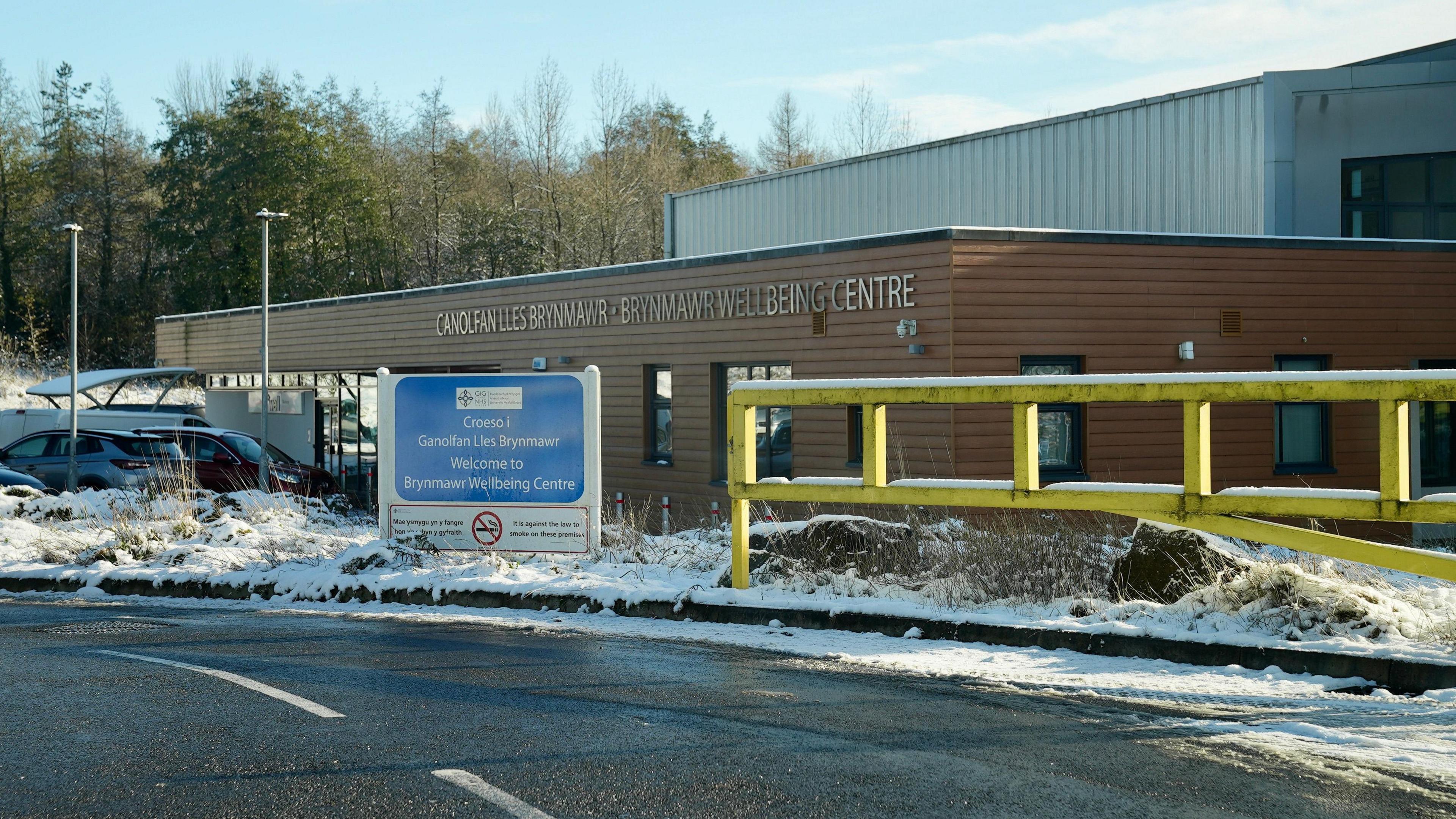 A picture of Brynmawr Medical Practice, which is a low, wooden building set in front of a large metal building.