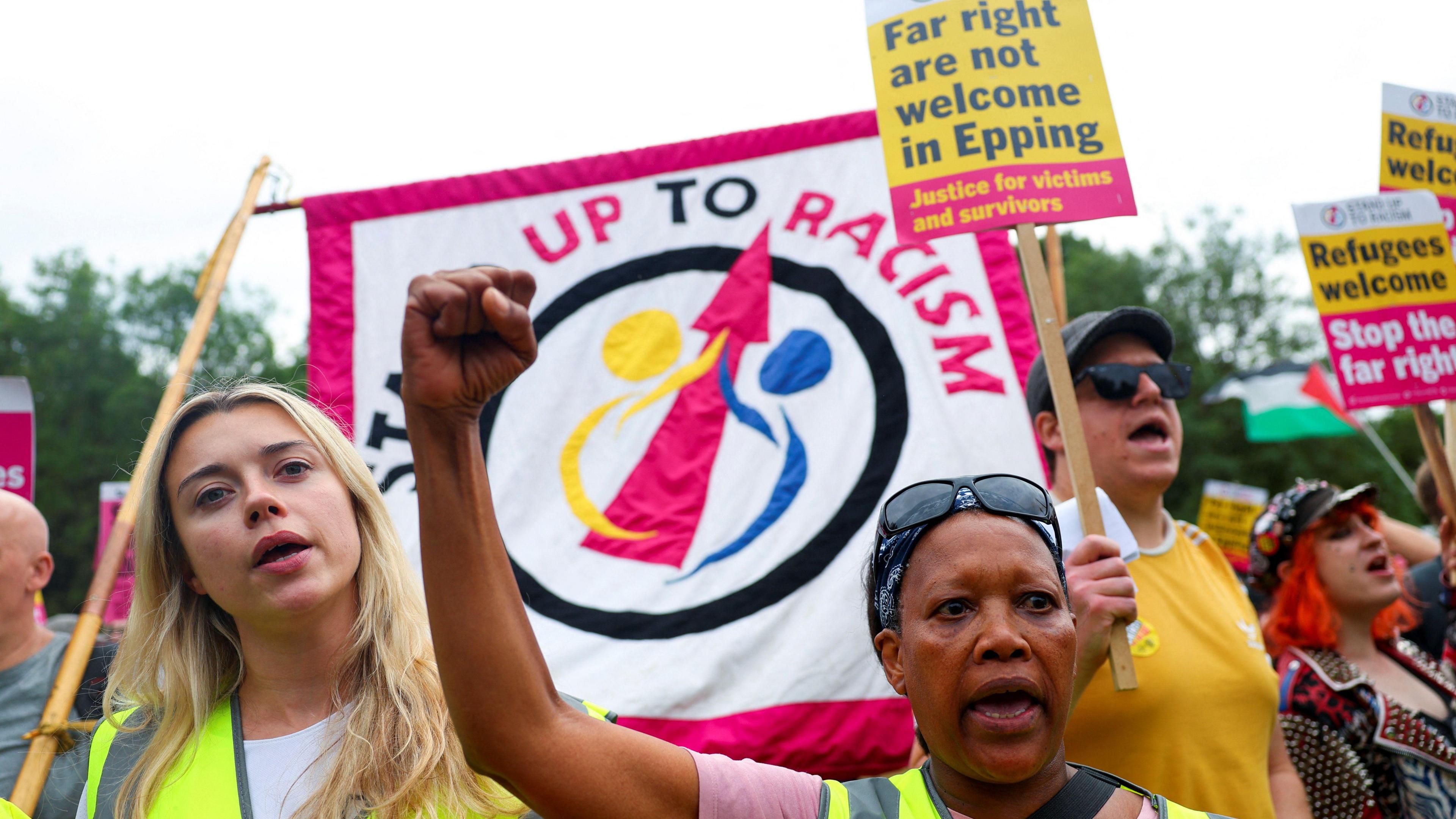 A crowd holds banners and signs, some of which read: "Stand up to Racism".