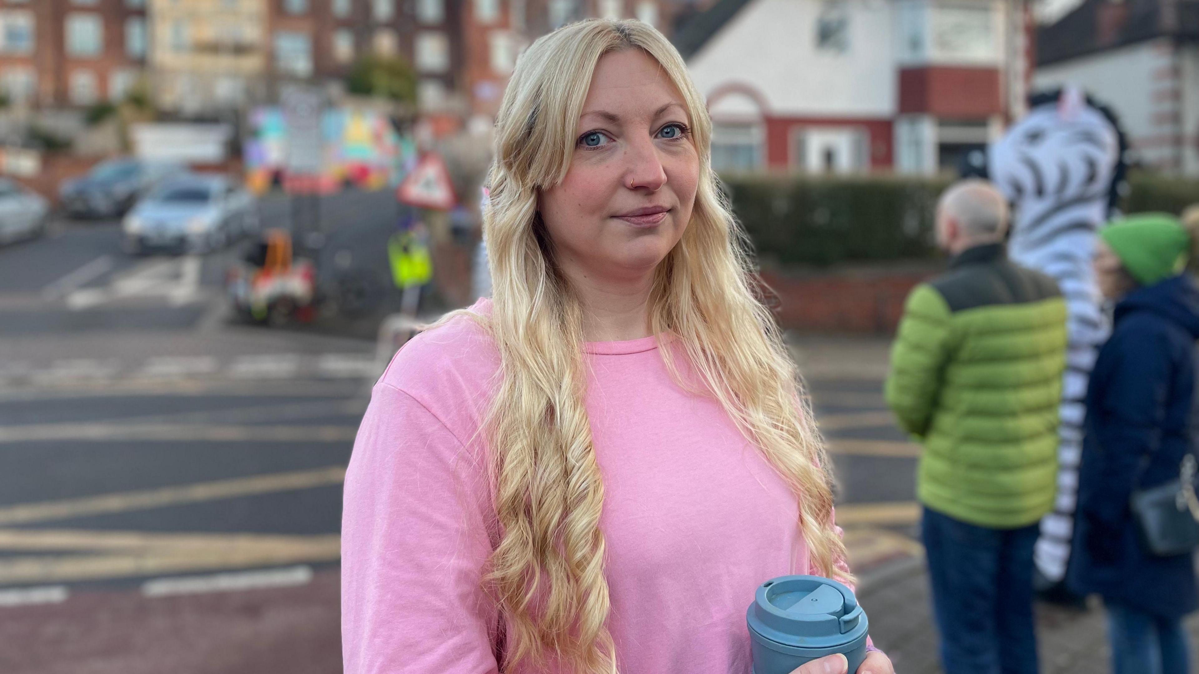 Eve Holdsworth, a woman with blonde hair wearing a pink shirt, is stood next to a road junction.