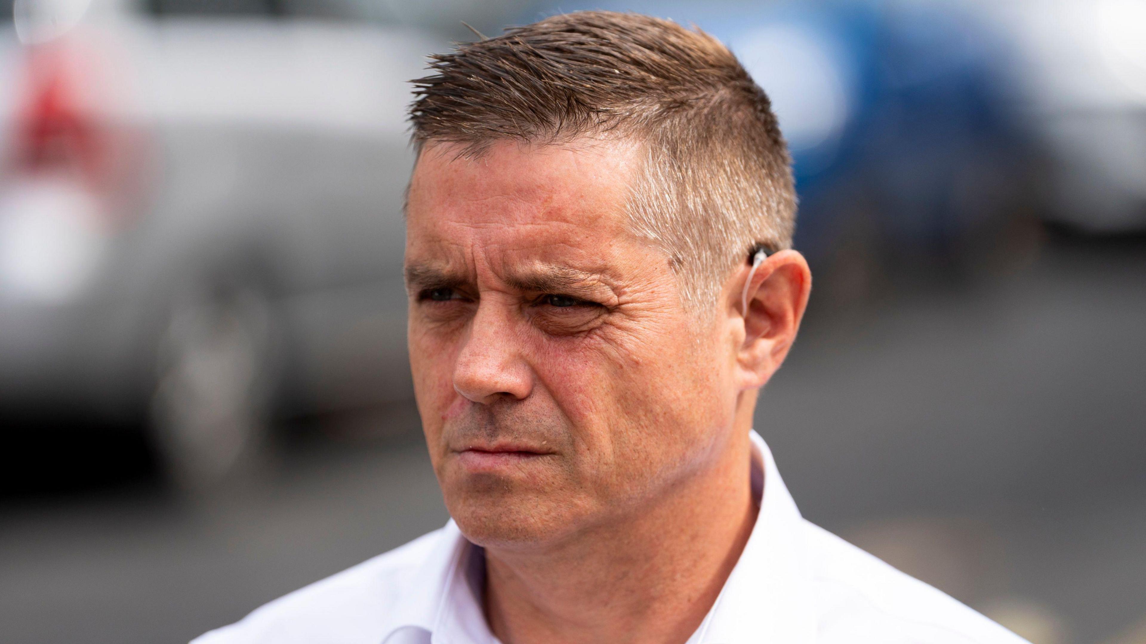 John Alford in a white shirt outside court, looking almost side-on, frowning. He is clean shaven. He has short hair, gelled into a quiff.