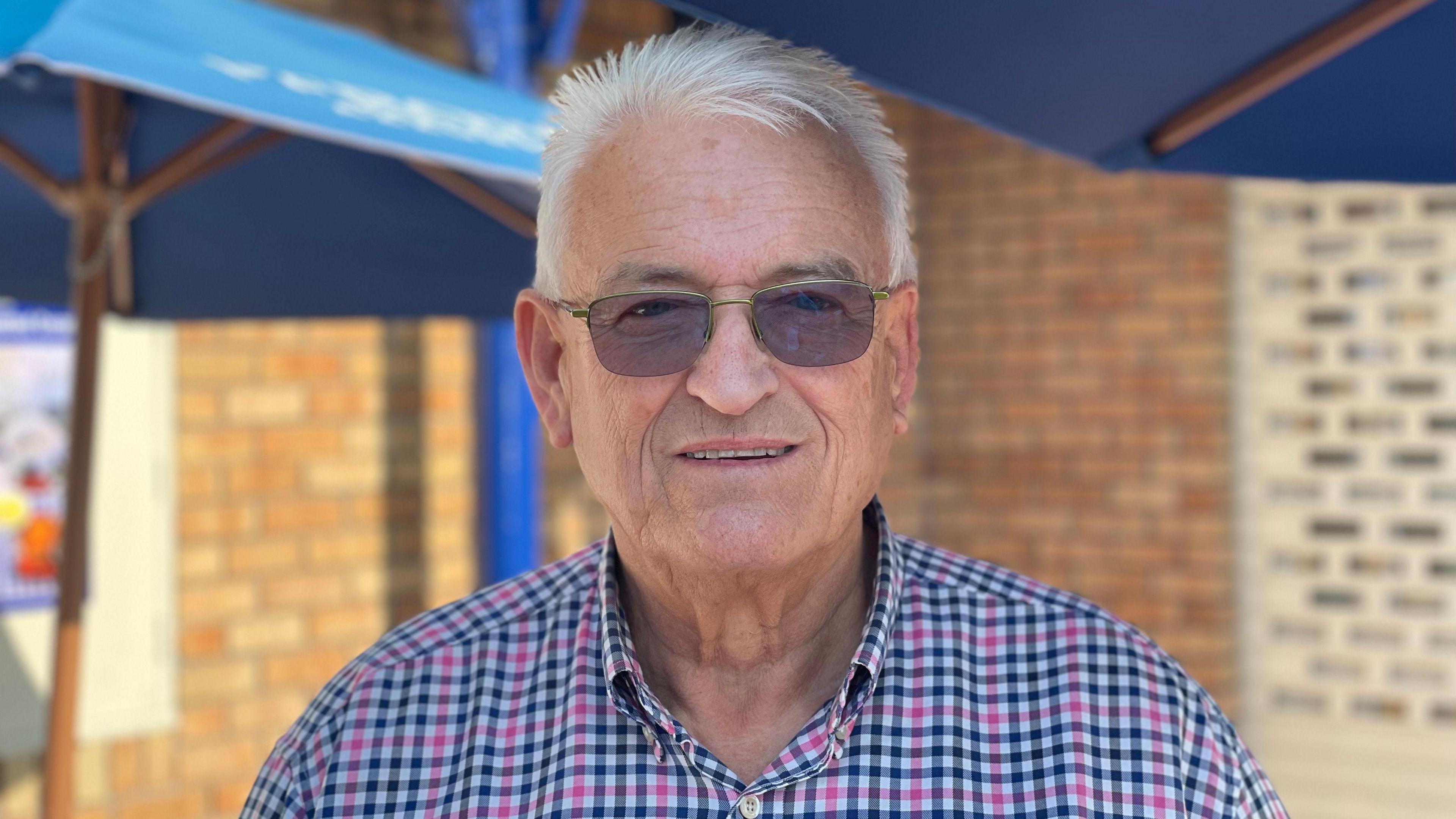 Dave Charles stands outside the Seafood Cafe in Town Gardens, Skegness. He has white hair and is wearing a navy and pink checked shirt and sunglasses.