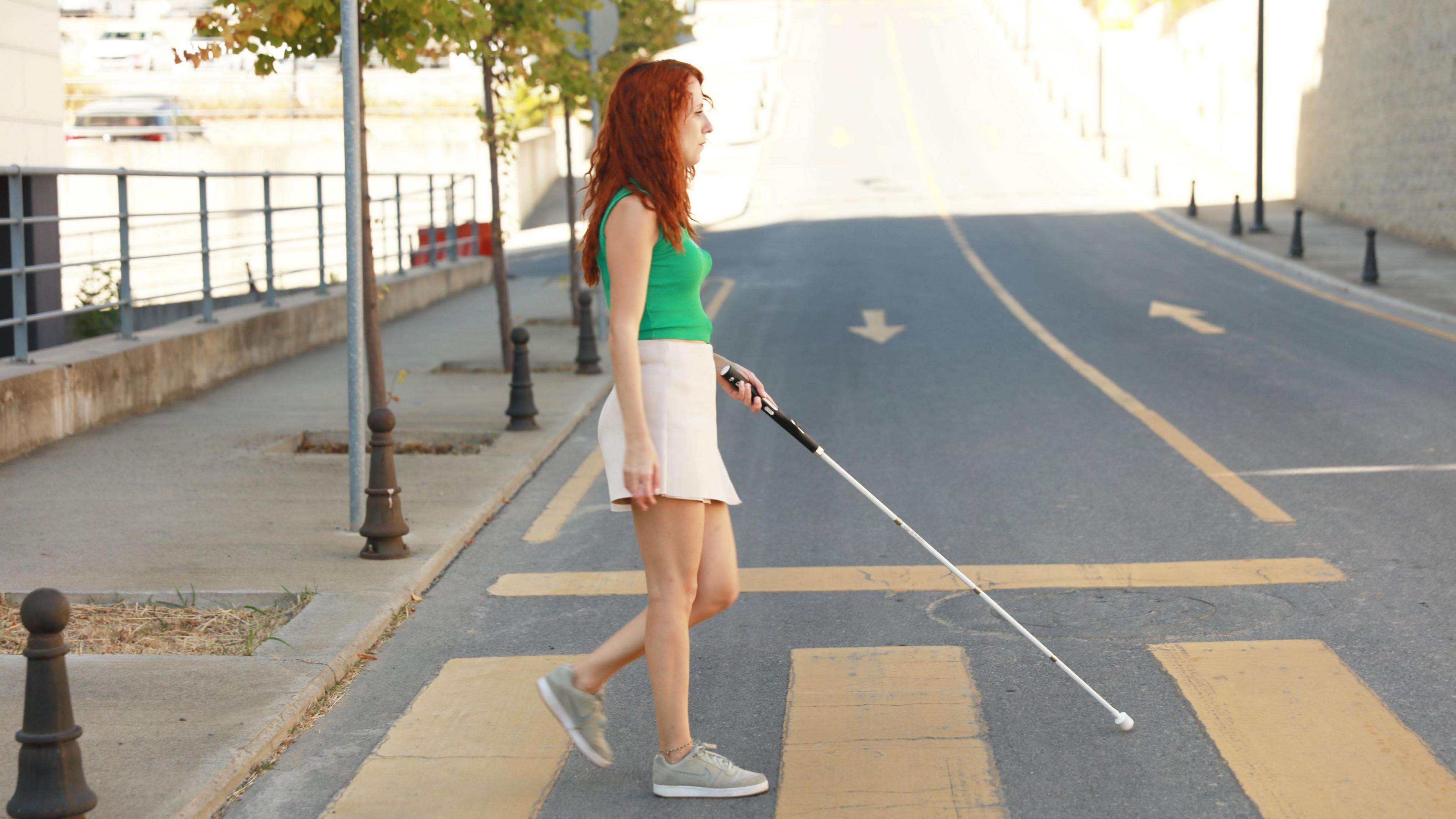 A lady holding a cane crosses a pedestrian crossing