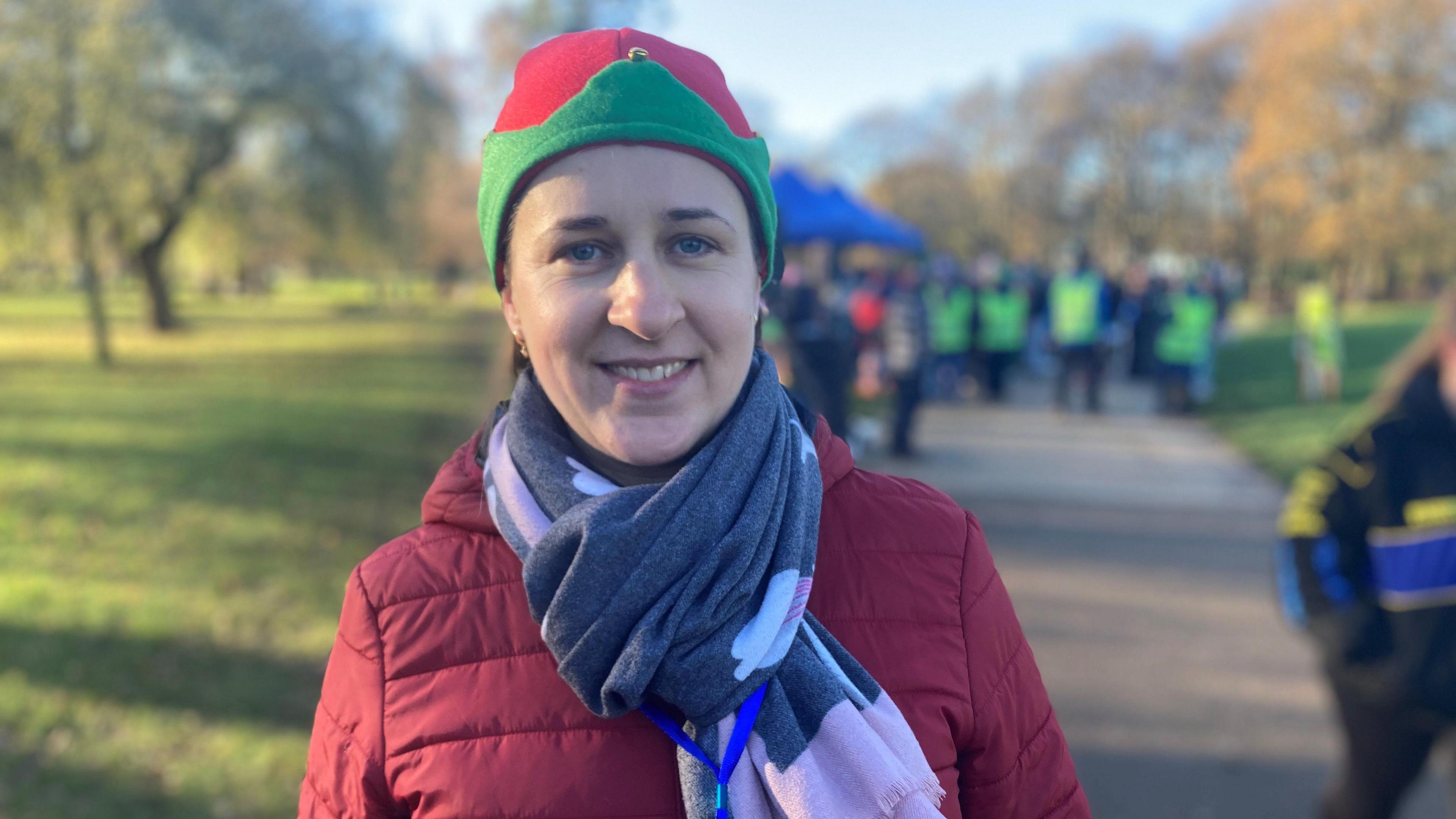 Jurate wears a green and red elf hat and a padded jacket and scarf. She smiles for the camera.