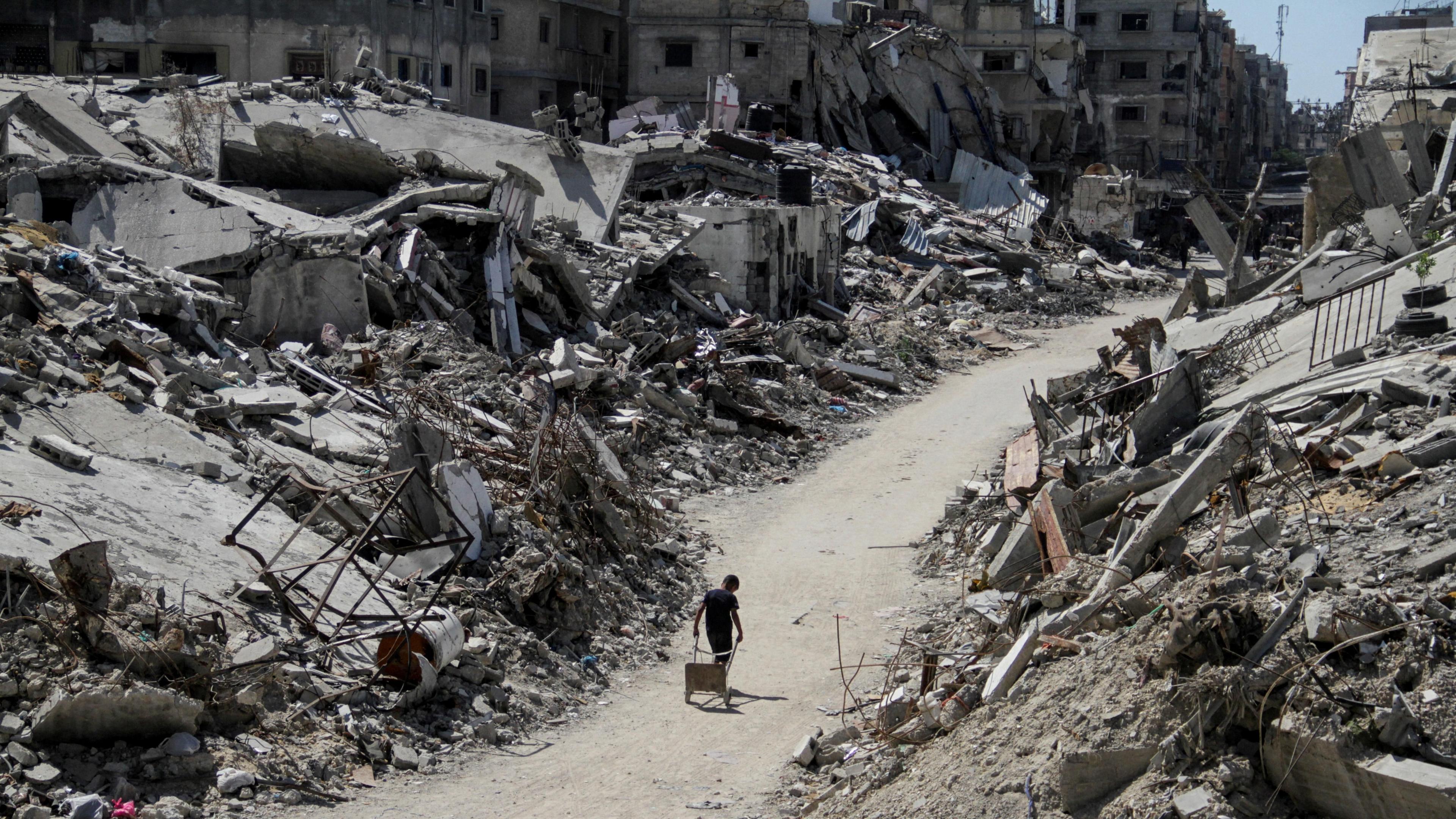 A lone Palestinian drags a trolley along a path between debris from destroyed buildings showing the devastation caused by the ongoing Israel-Gaza conflict