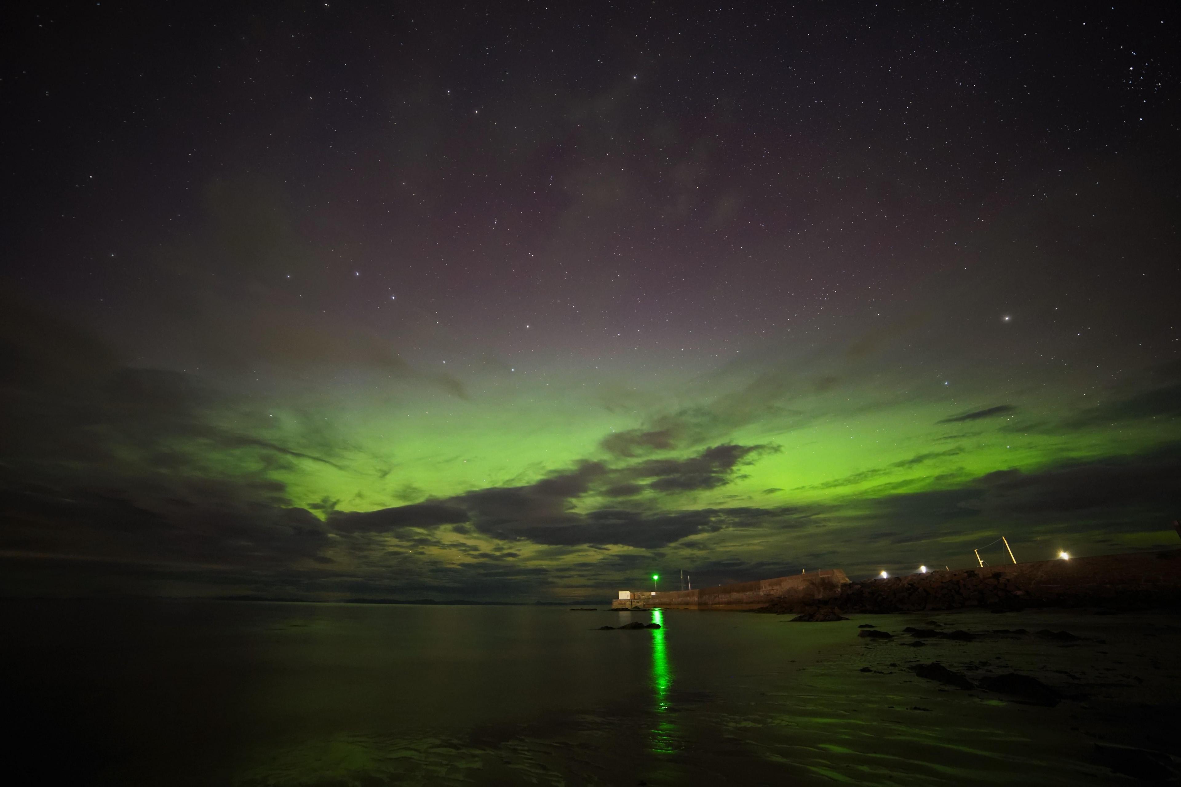 A starry sky plays host to a striking green light show off the coast of Hopeman. A green light from a marker on the harbour, and the glow of lights on the shore are also visible.