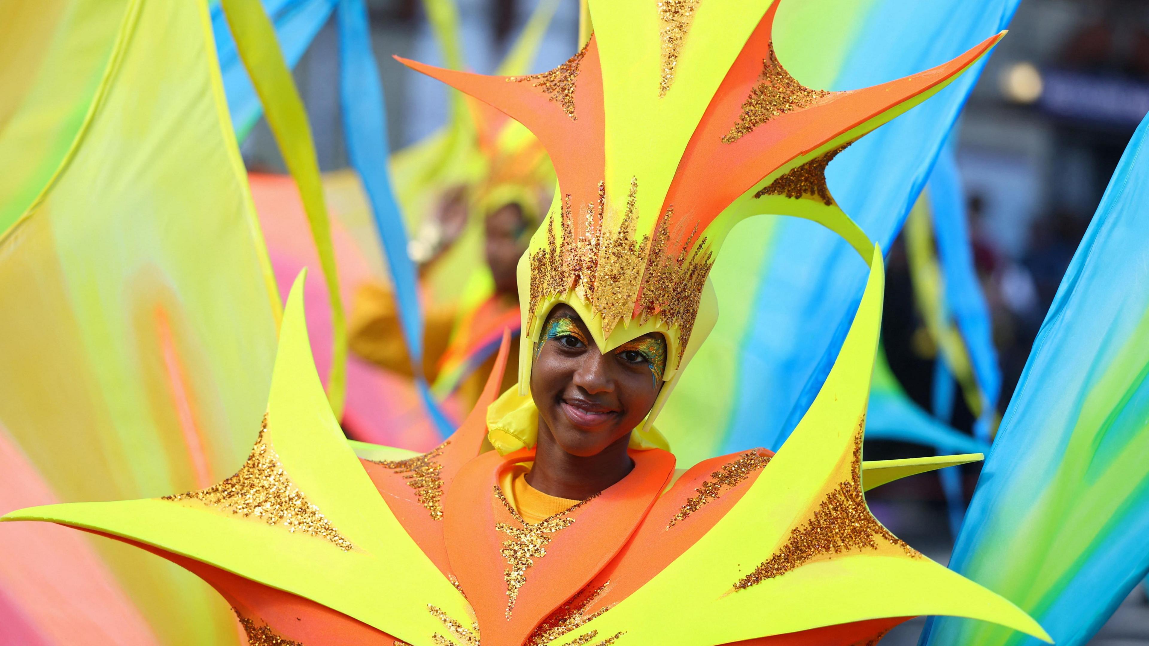 A child in an orange and yellow costume smiles during the parade.