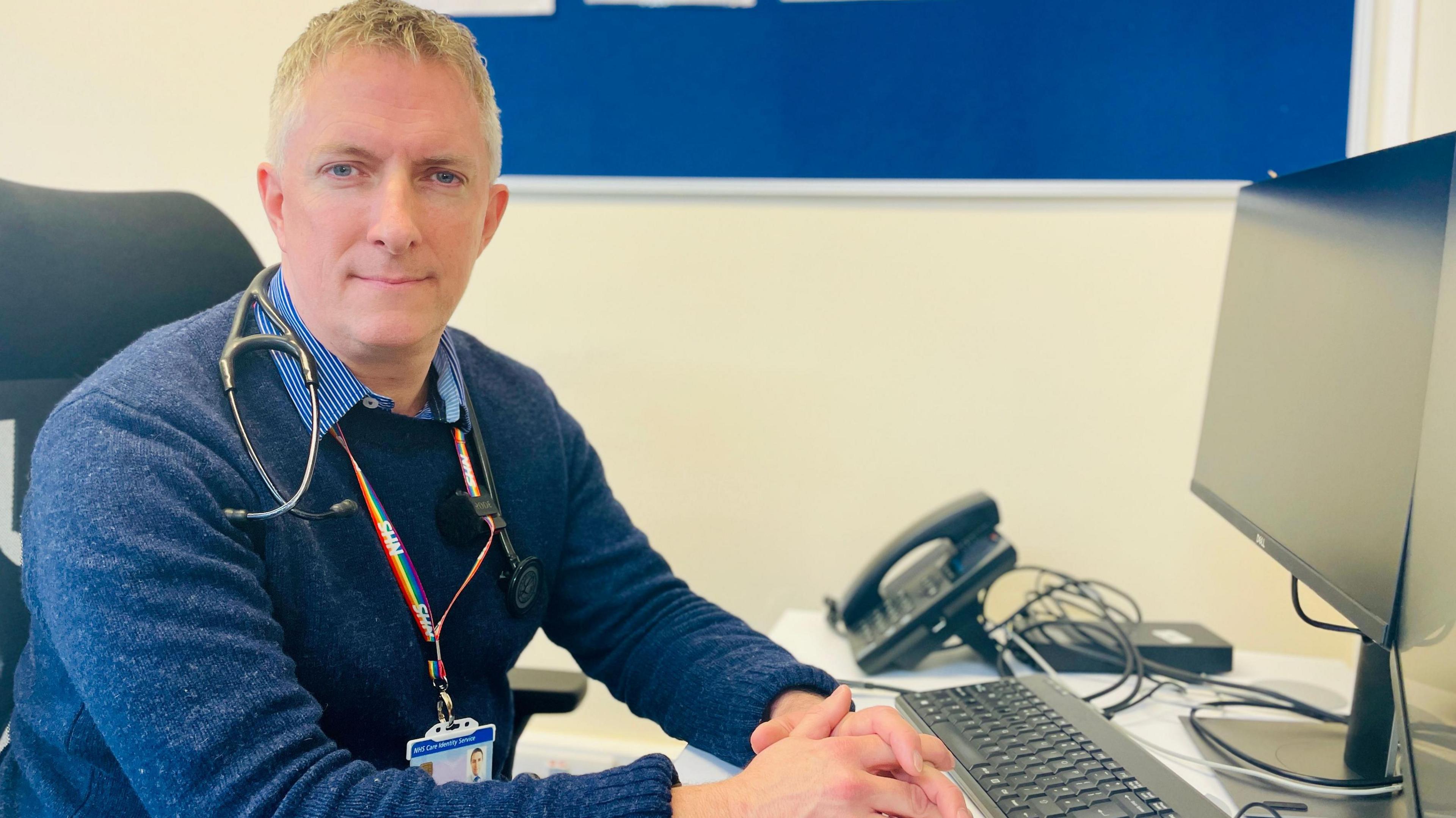 Dr James Simpkin, a Brighton GP, sitting at his desk in front of a computer and looking at the camera
